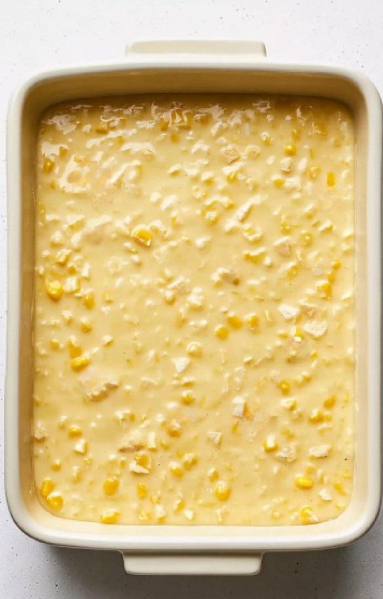 Baking dish with creamy corn mixture for scalloped corn casserole, an old-fashioned comfort food side.