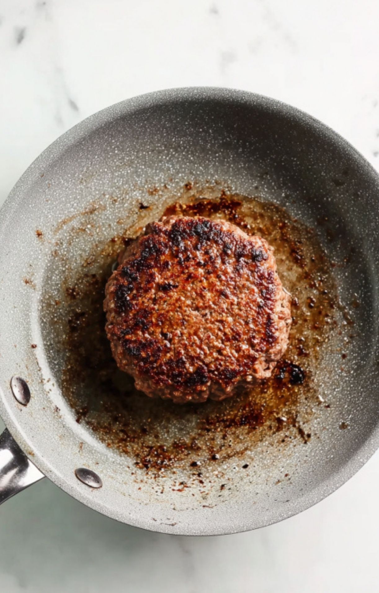 Seared beef patty in a skillet, perfectly browned and juicy. This is the delicious filling for a homemade Beef Wellington, a favorite for cozy winter dinners.