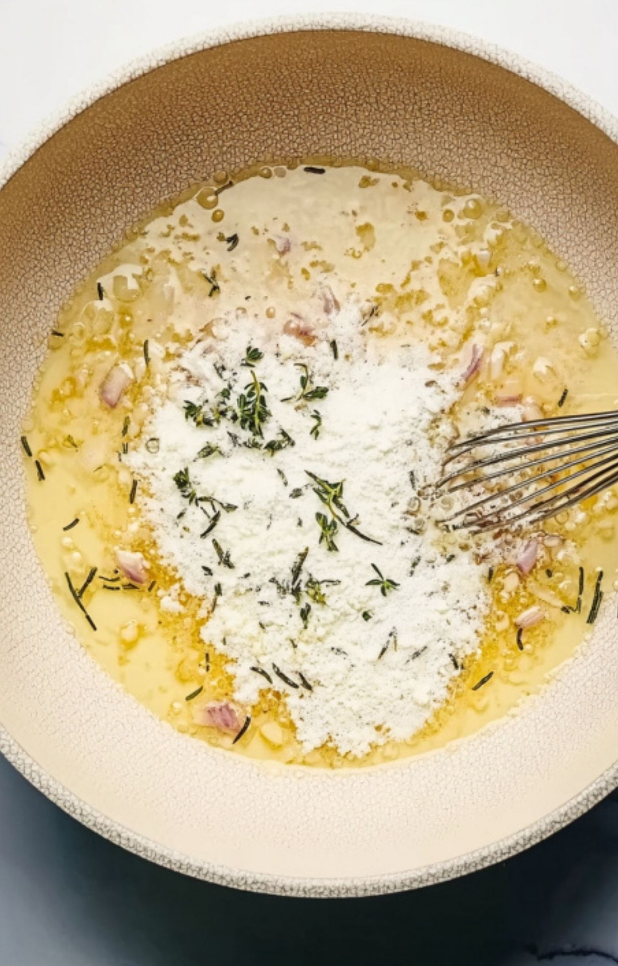 Whisking flour and fresh herbs into the sauce, showing how to make a thick, savory red wine sauce for beef wellington or holiday roast.