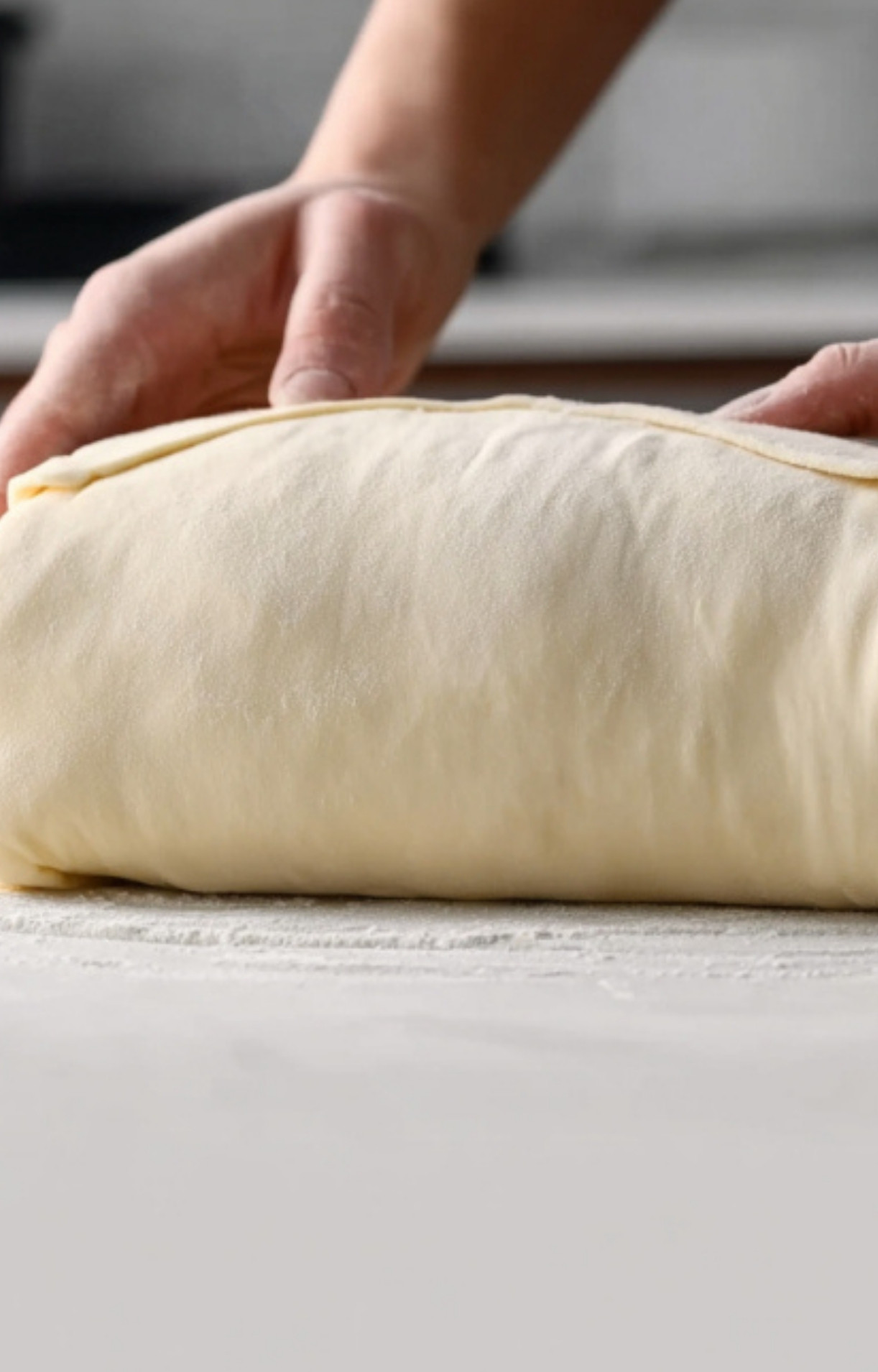 Hands wrapping beef tenderloin in pastry dough, a key step for assembling sous vide beef wellington at home.