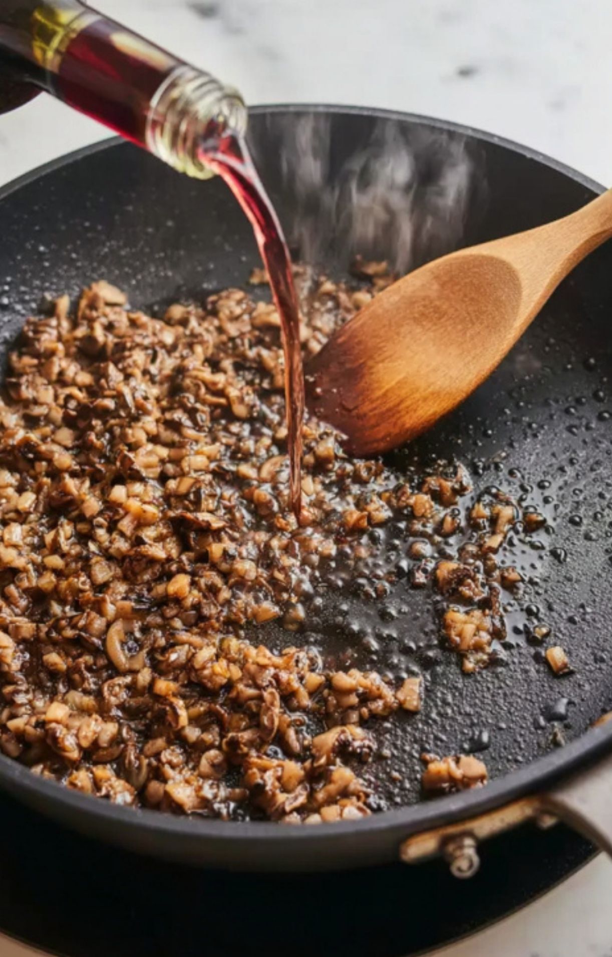 Red wine being poured into a skillet of finely chopped mushrooms and shallots, creating the rich duxelles filling for classic beef Wellington.