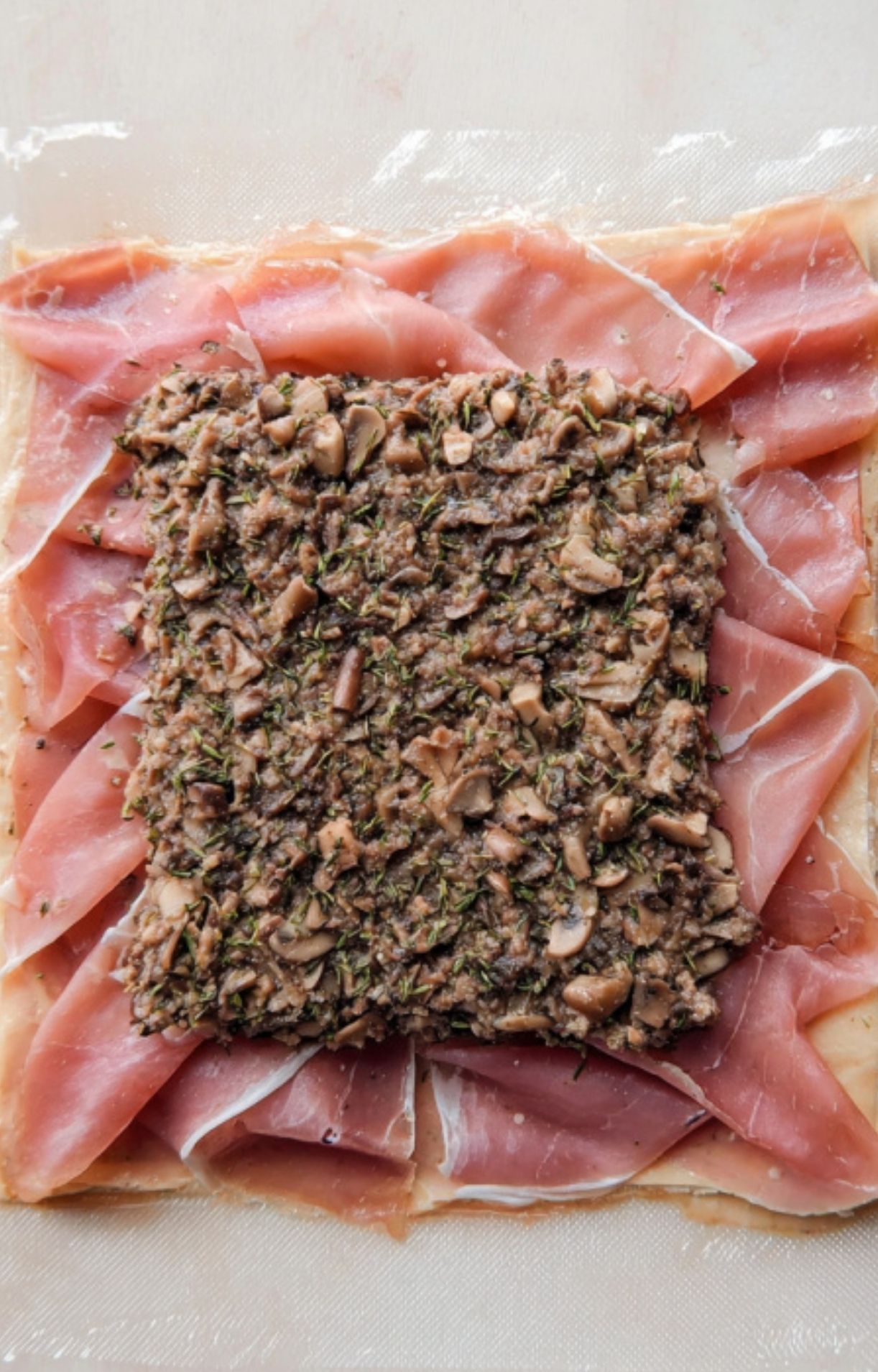 Layer of prosciutto and mushroom-chestnut duxelles on pastry, ready to wrap around beef for Christmas Beef Wellington. Flavorful holiday step.