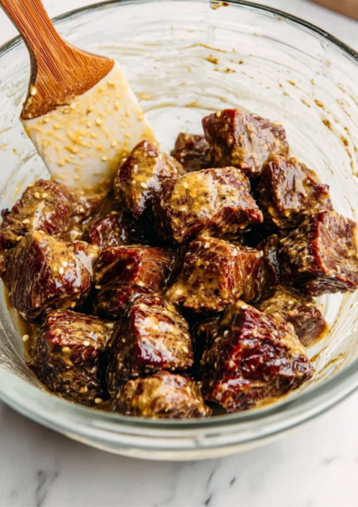 Beef tenderloin cubes coated in mustard marinade in a glass bowl, perfect for making tender mini beef wellington bites.