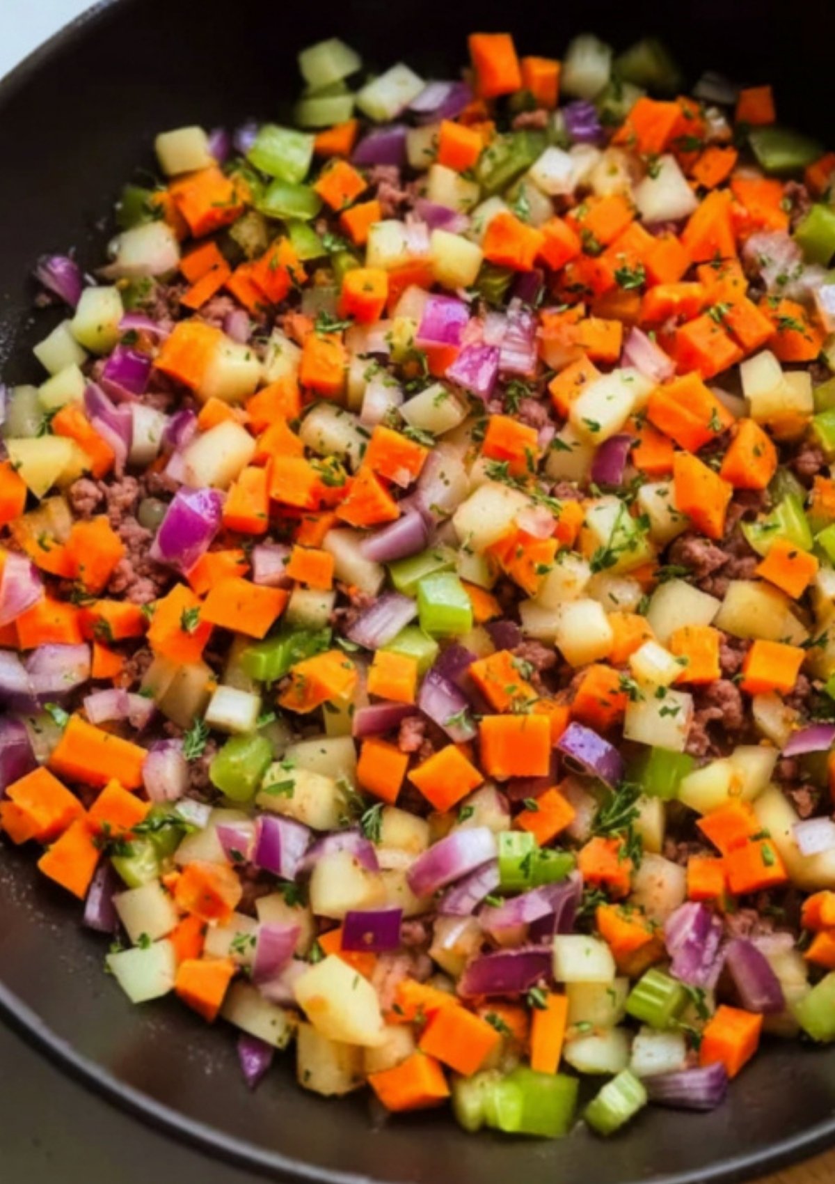 Chopped carrots, potatoes, celery, and red onions sautéed in a skillet, ready for ground beef wellington assembly.