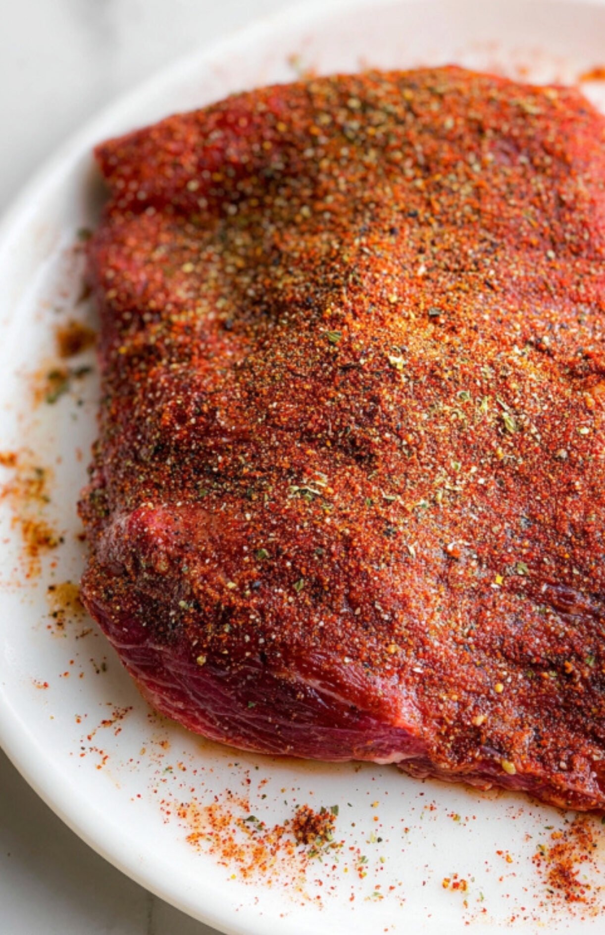 Flank steak coated generously with homemade dry rub, prepped for smoking and grilling, great for a flavorful summer meal.