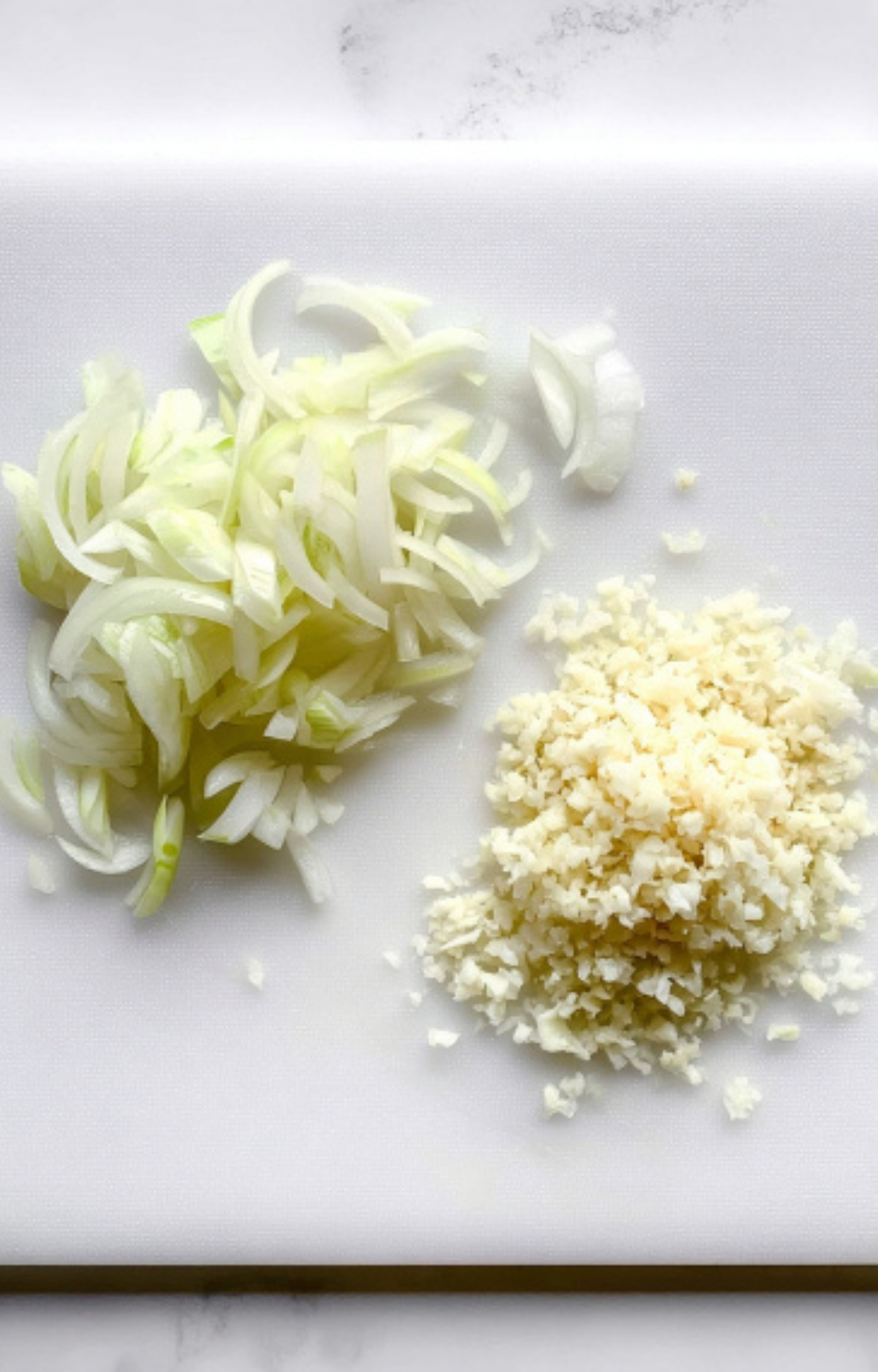 Sliced yellow onions and minced garlic prepped on a white cutting board for homemade Salsberry Steak With Mushroom Gravy, perfect for hearty comfort food recipes and easy weeknight dinners.