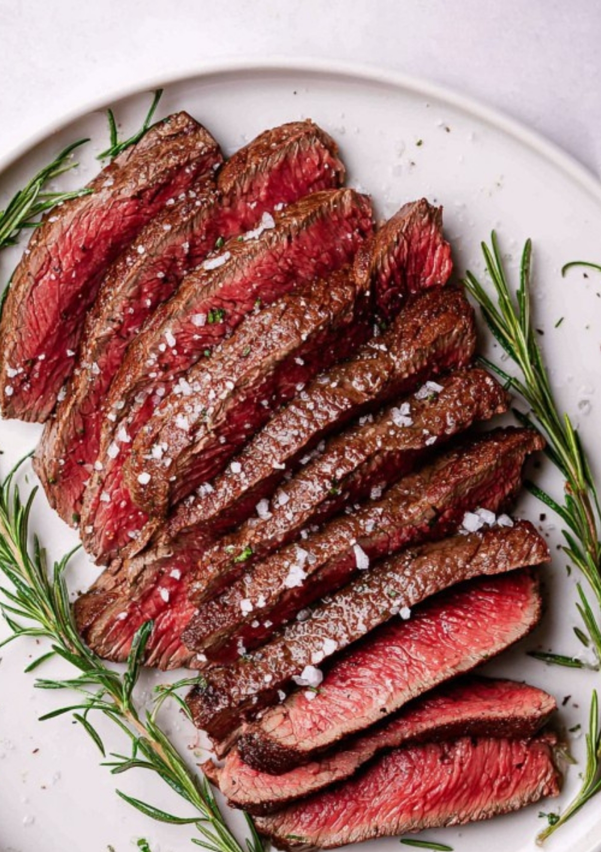 Perfectly cooked medium rare round steak sliced on a white plate with rosemary, made for easy skillet dinners and high protein meal ideas.