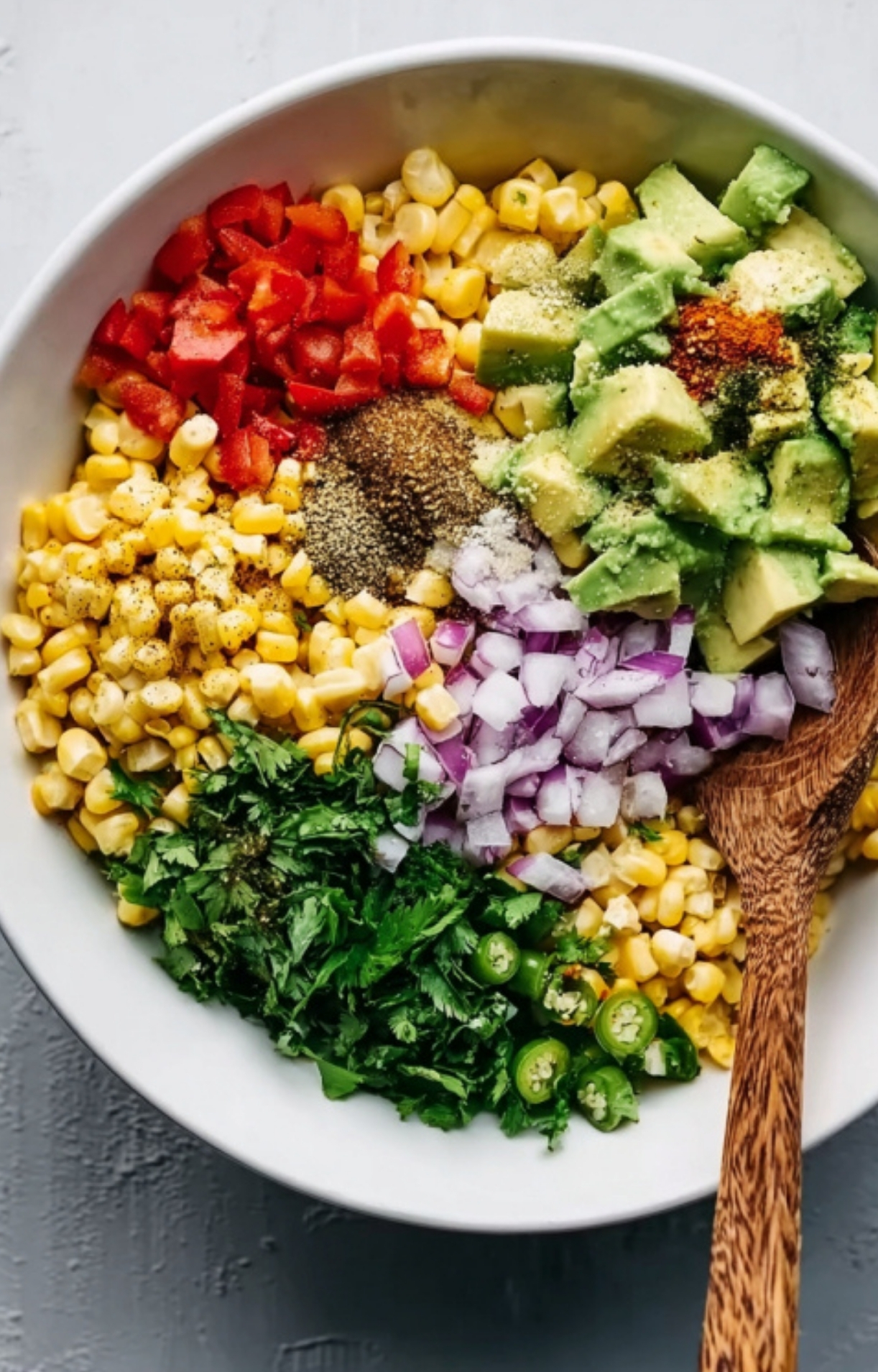 Bowl of fresh corn, diced avocado, red onion, jalapeño, cilantro, and spices ready to be mixed for salsa.