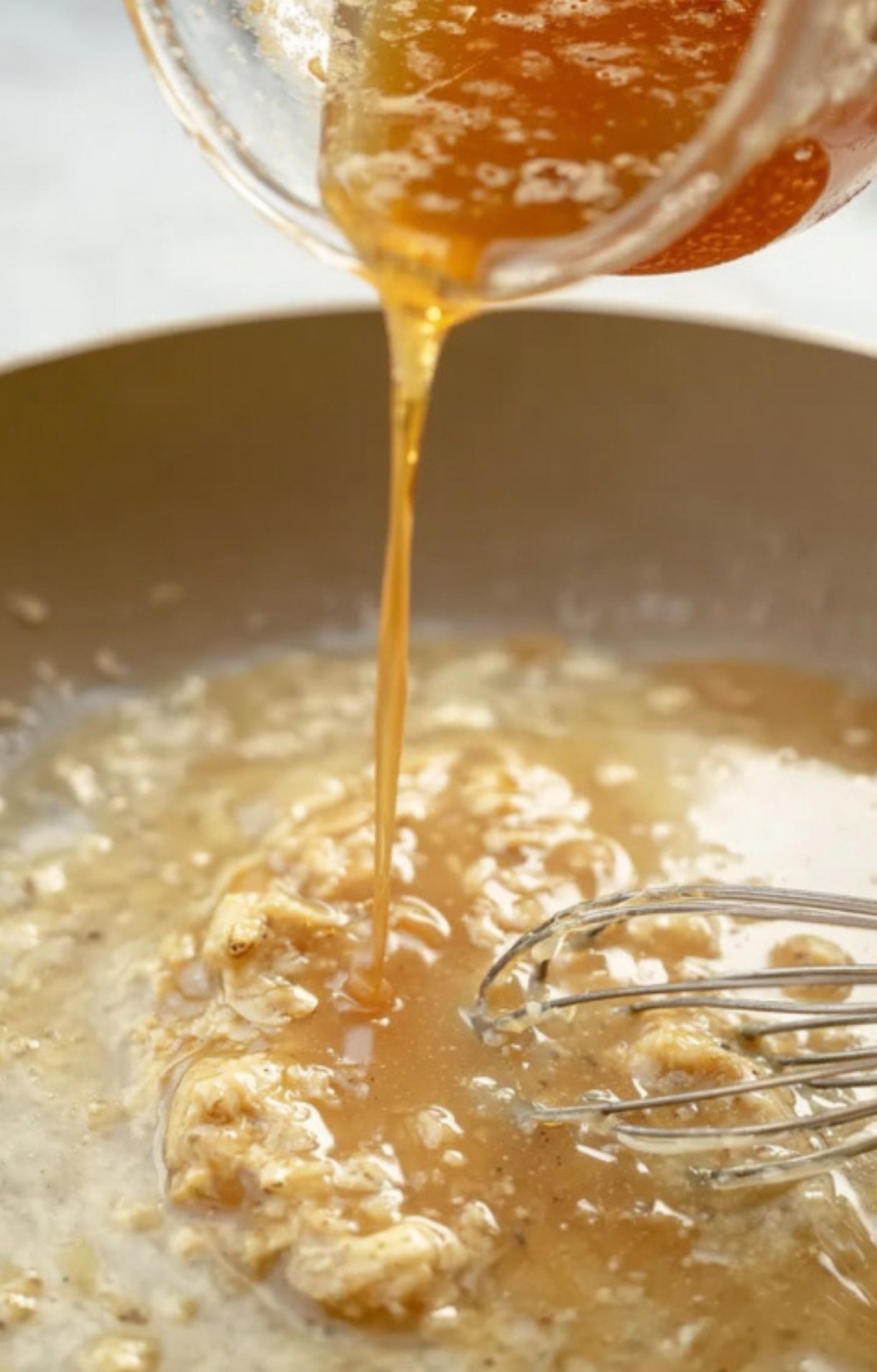 Stream of broth being poured into a skillet with roux as a whisk mixes to form gravy.