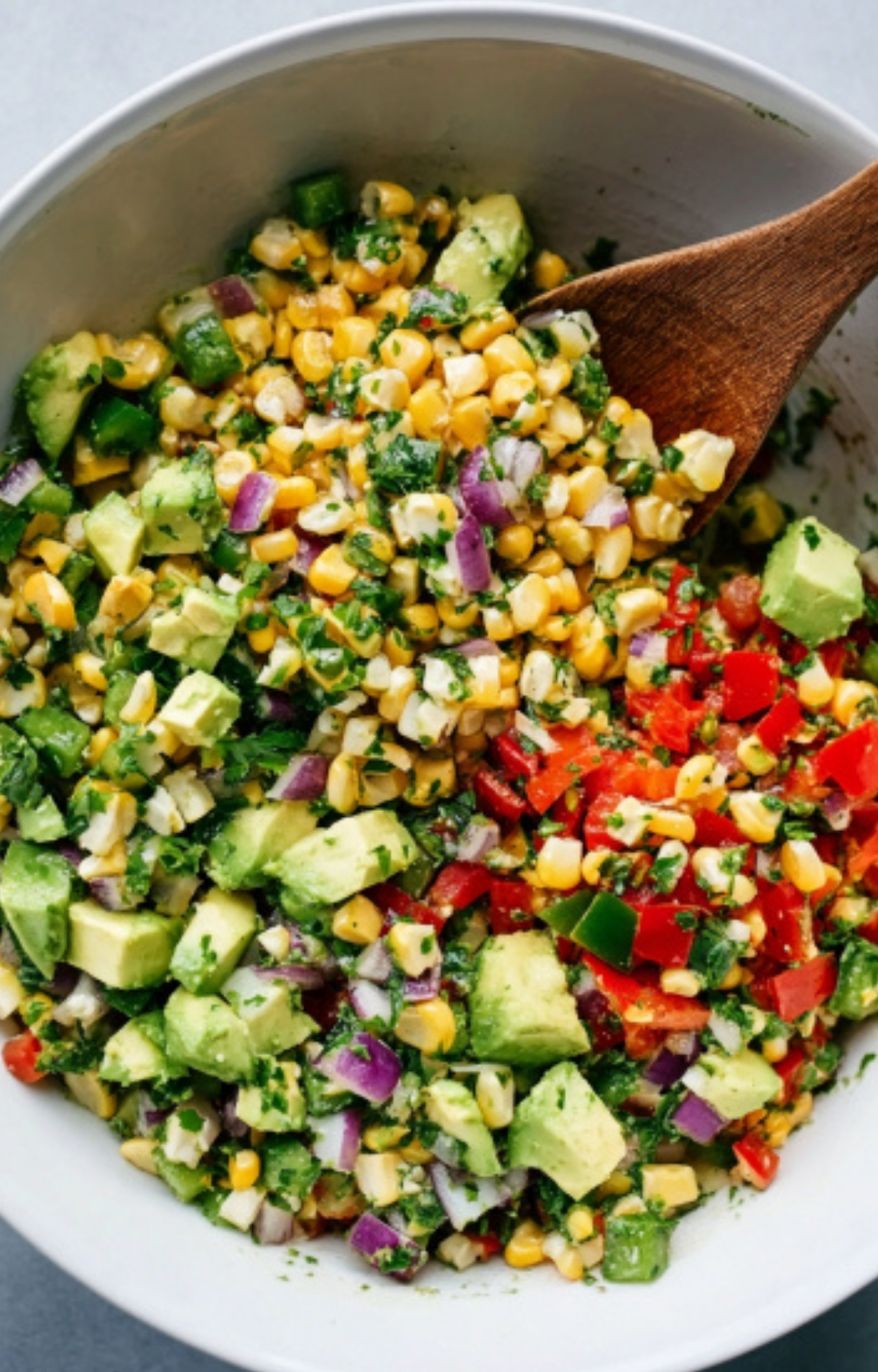 Corn, avocado, red onion, and bell pepper being mixed for a bright, healthy salsa.