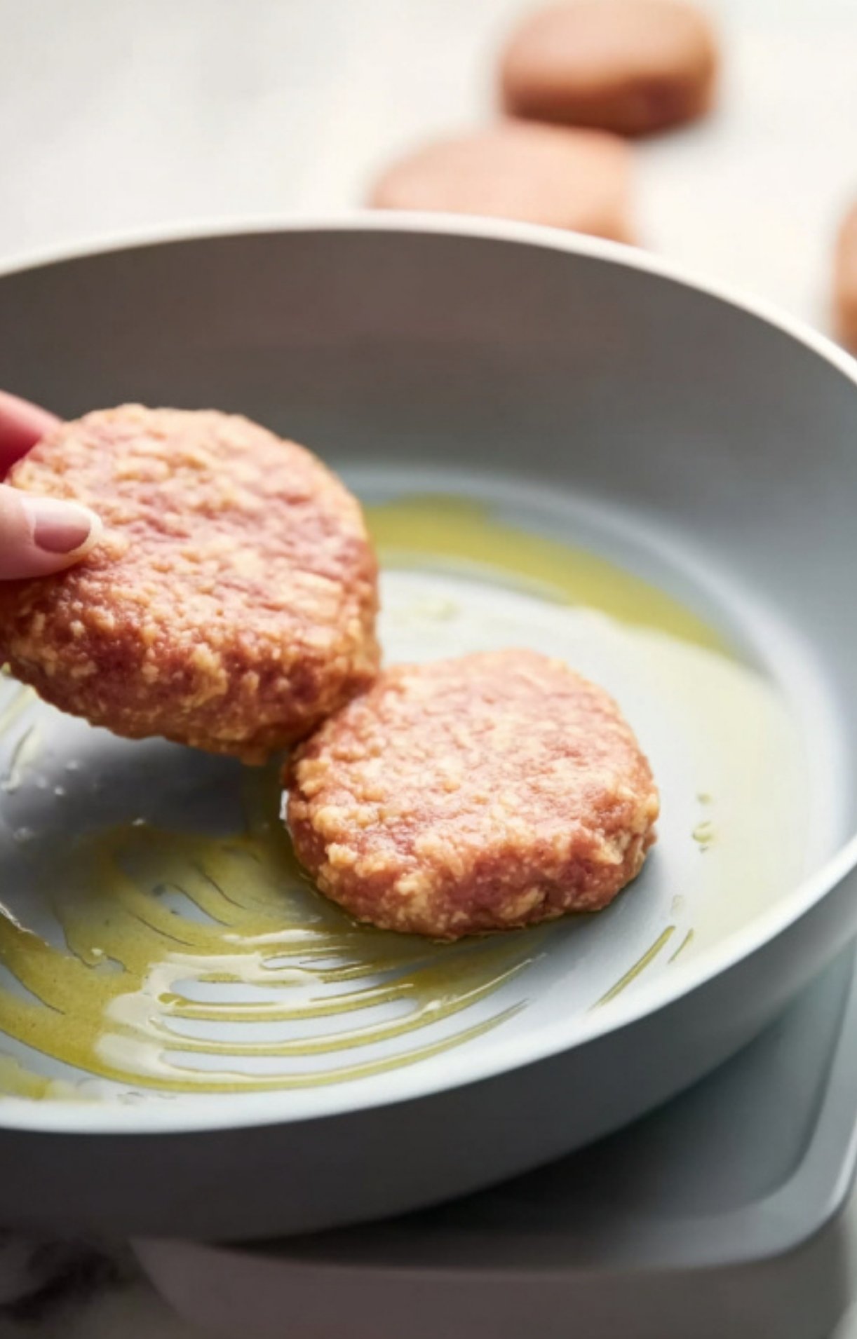 Hand placing raw ground turkey Salisbury steak patties into an oiled skillet before cooking.