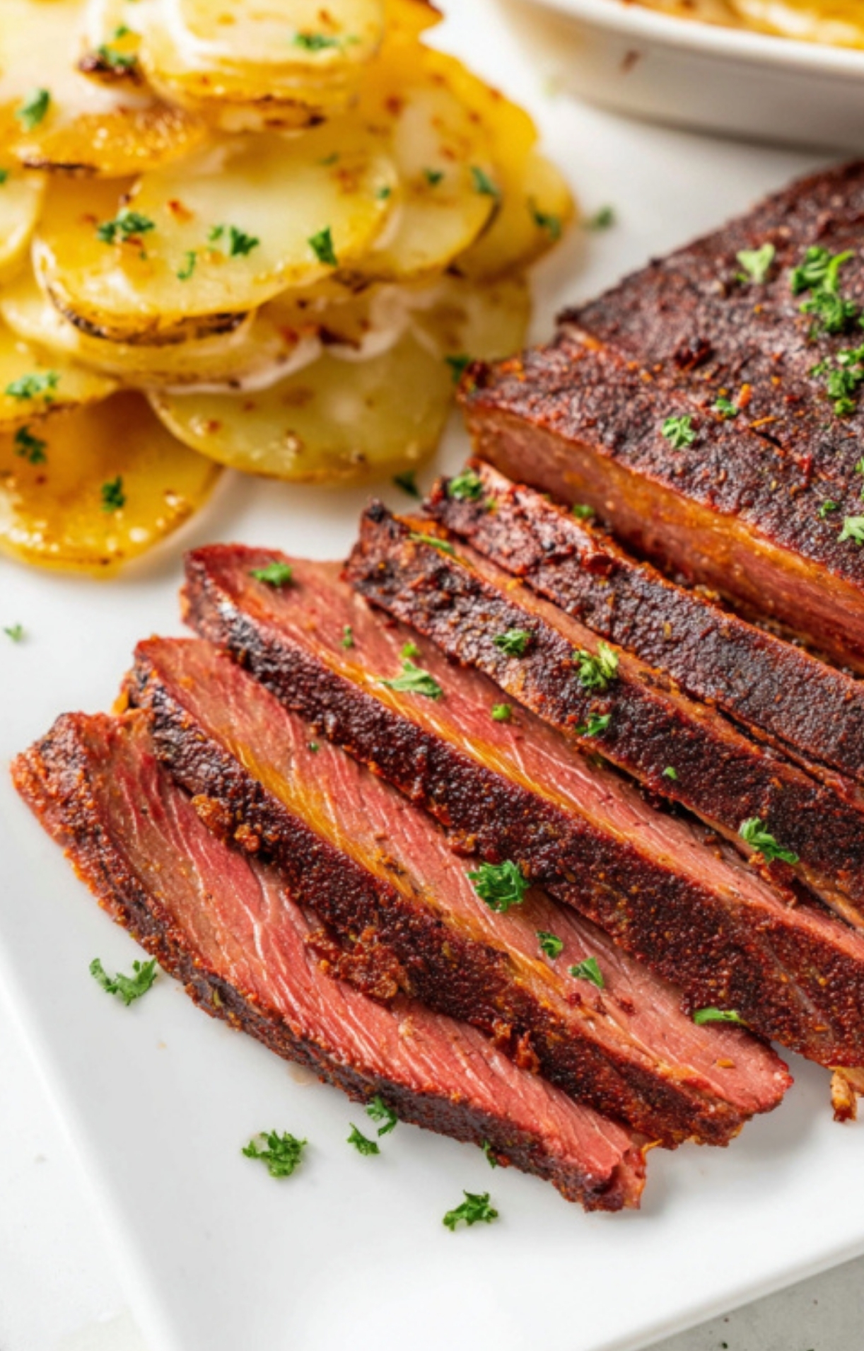 Slices of smoked flank steak paired with golden potatoes on a white plate, ideal for an easy weeknight meal or backyard BBQ.