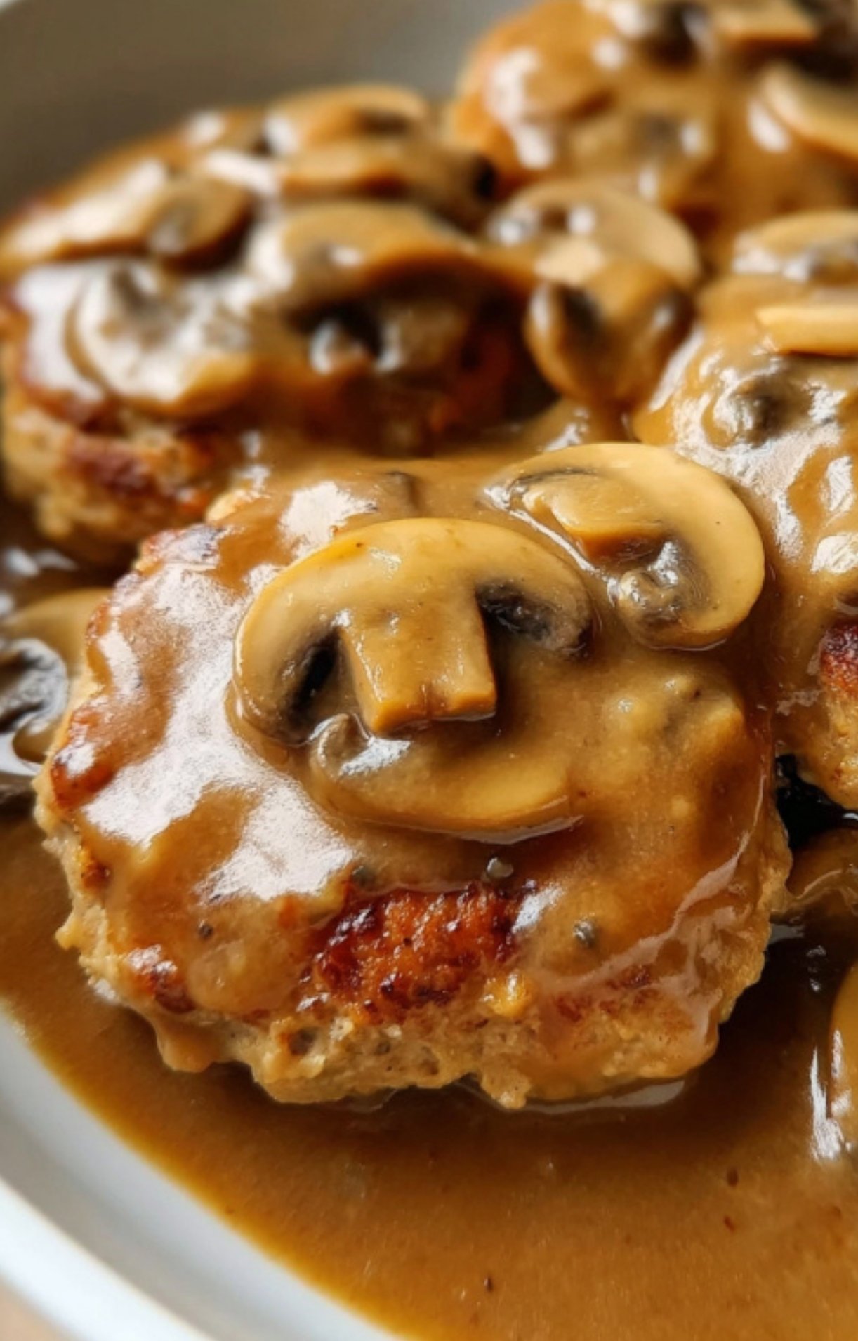 Close-up view of golden-browned turkey Salisbury steak patties covered in rich mushroom gravy with sliced mushrooms.