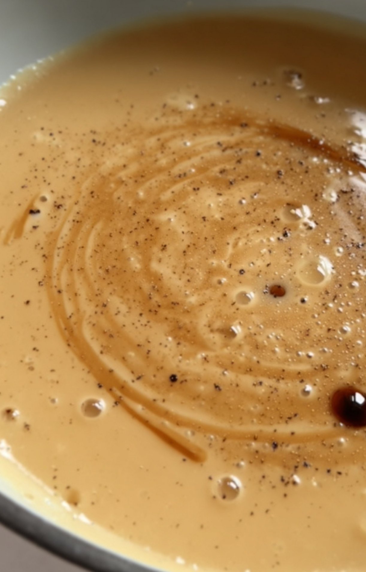 Thick, creamy brown gravy in a skillet with visible pepper and seasoning swirled throughout.