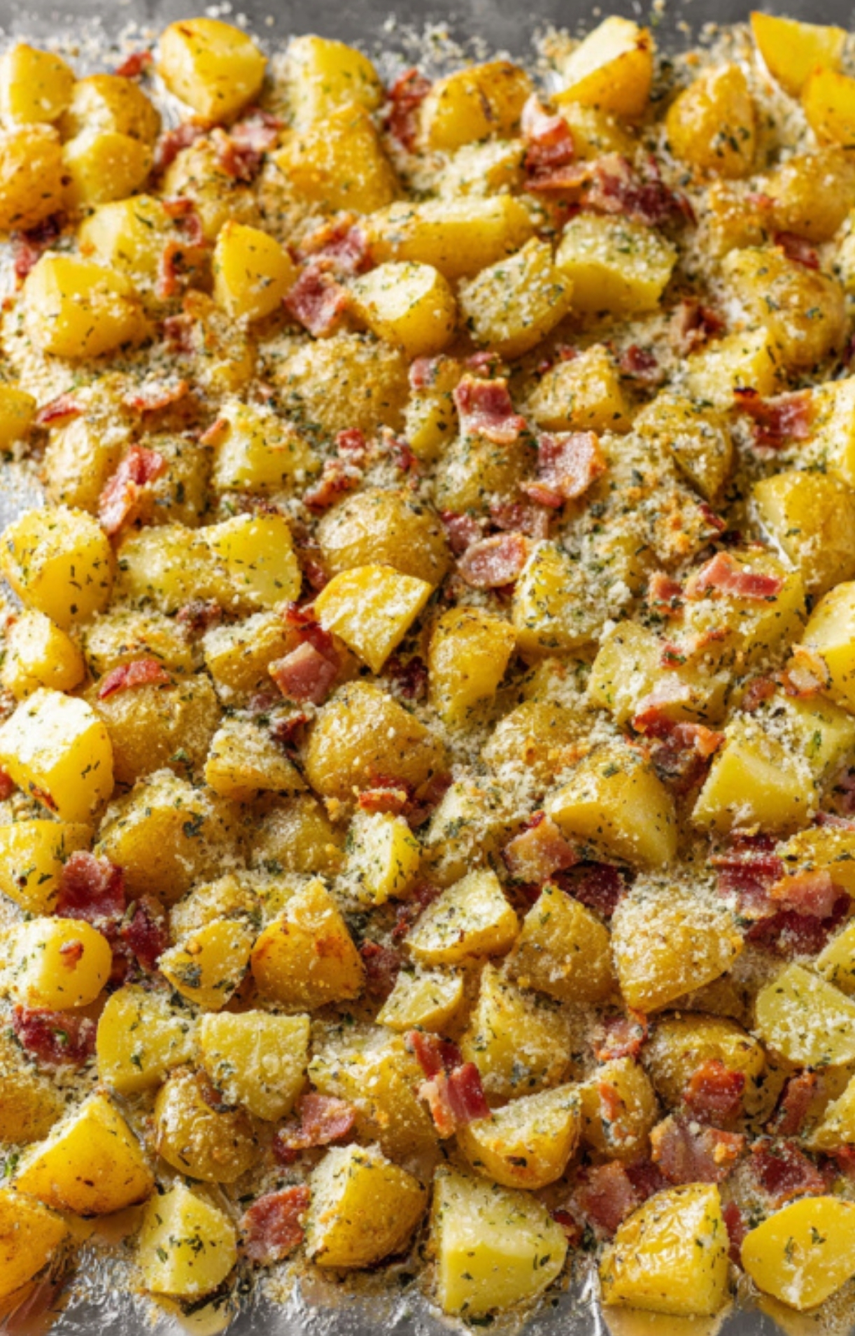 Roasted potatoes and bacon spread on a baking sheet, ready to be seasoned and topped with cheese for cheesy bacon ranch potatoes.