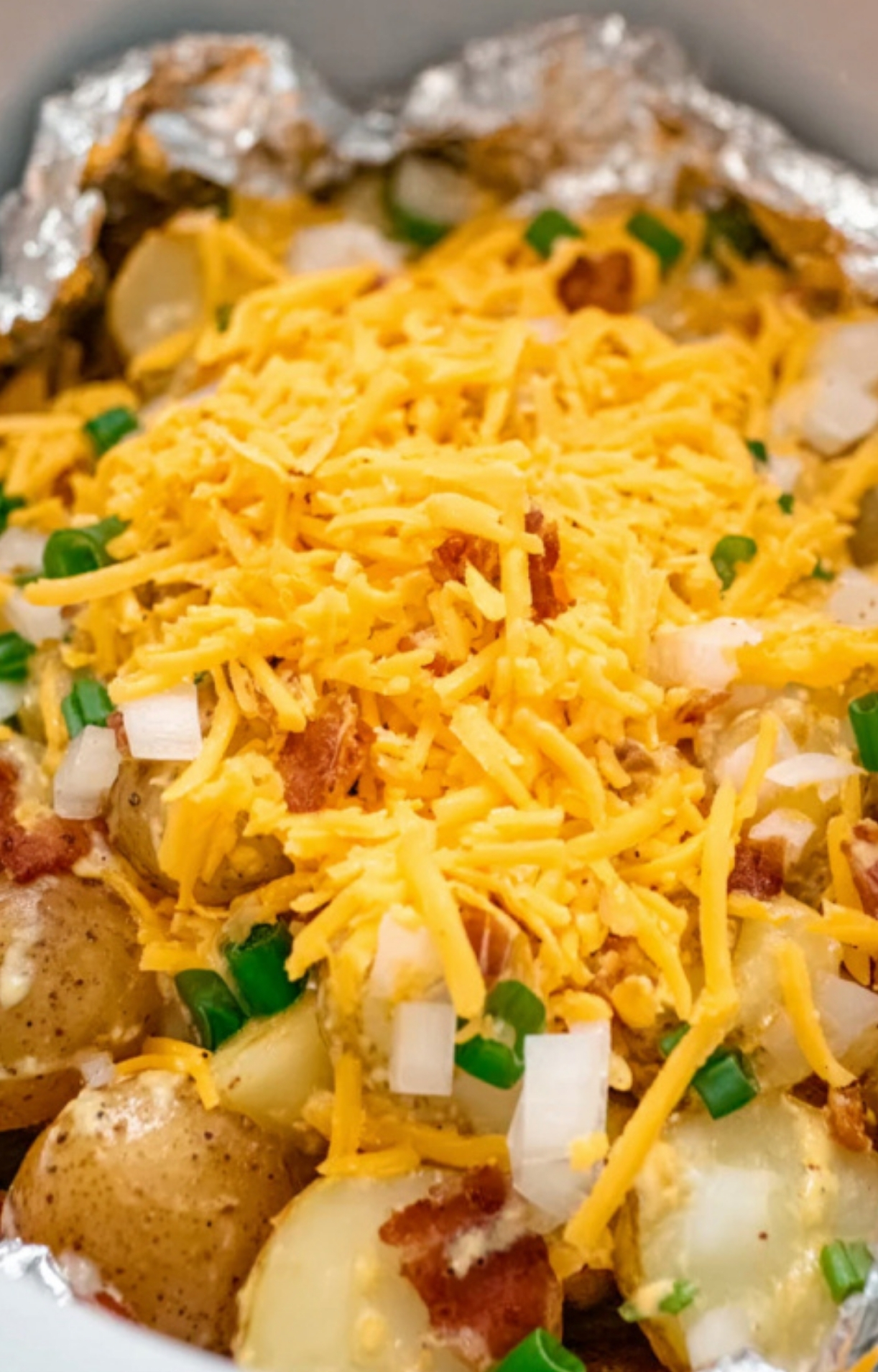 Close up of slow cooker cheesy bacon ranch potatoes topped with shredded cheddar, bacon, and green onions, perfect for a cozy crockpot side dish.