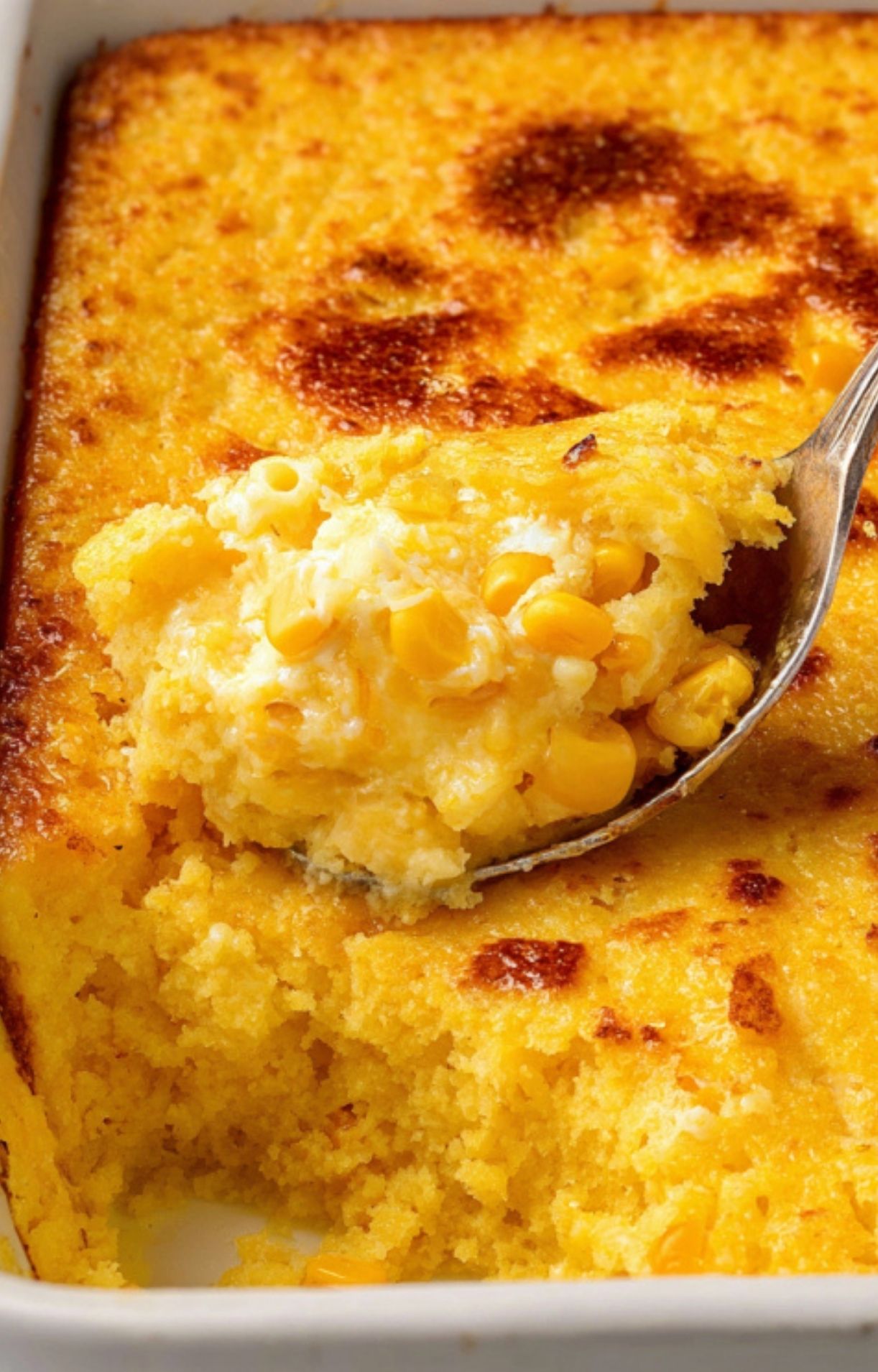 Spoonful of creamy, homemade corn pudding casserole with baked golden edges, showing rich texture and sweet corn kernels. Easy comfort food for holidays and Sunday dinner.