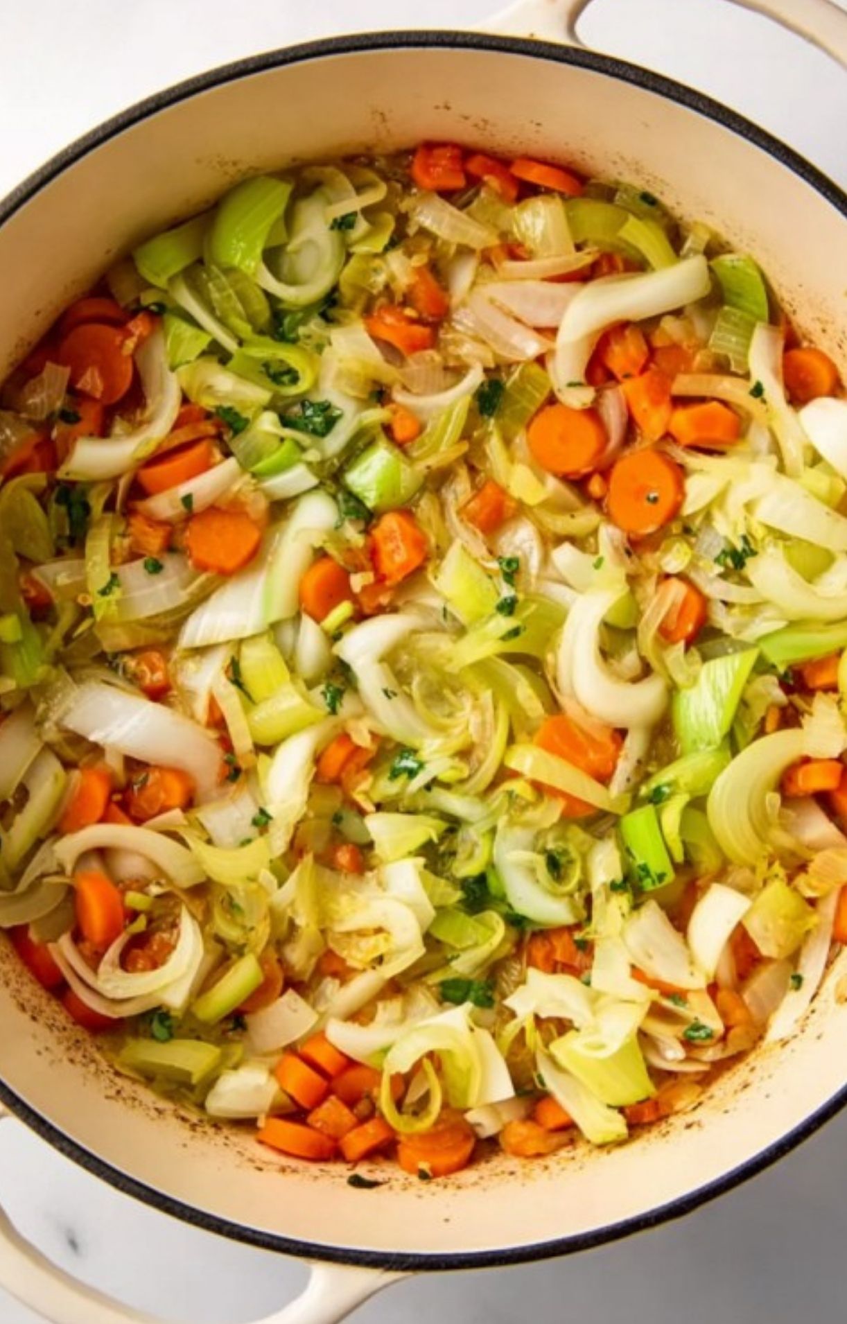 Chopped carrots, onions, leeks, and parsley sautéing in a Dutch oven as the base for a hearty cassoulet stew.