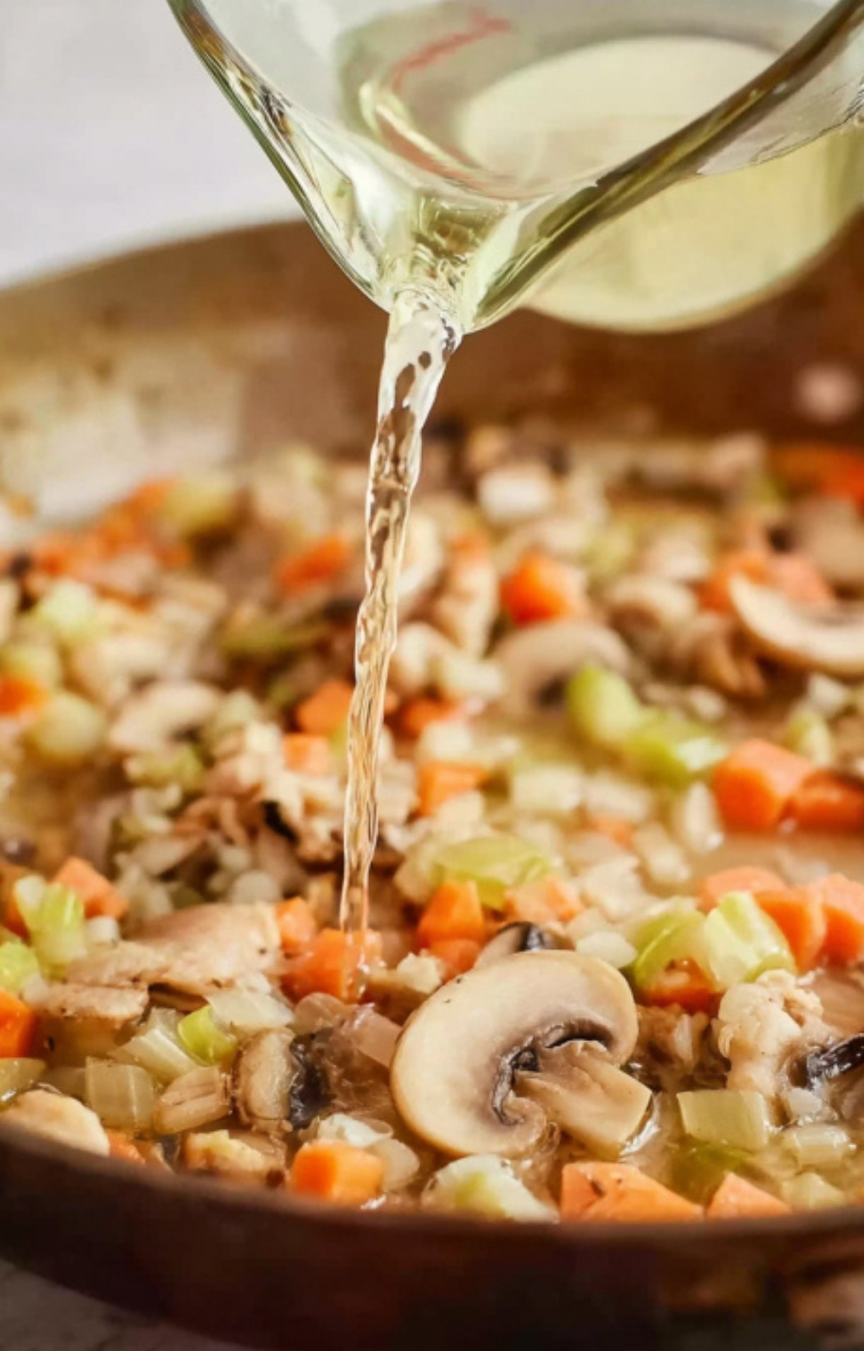 Pouring white wine into sautéed mushrooms, carrots, celery, and onions for fricassee.