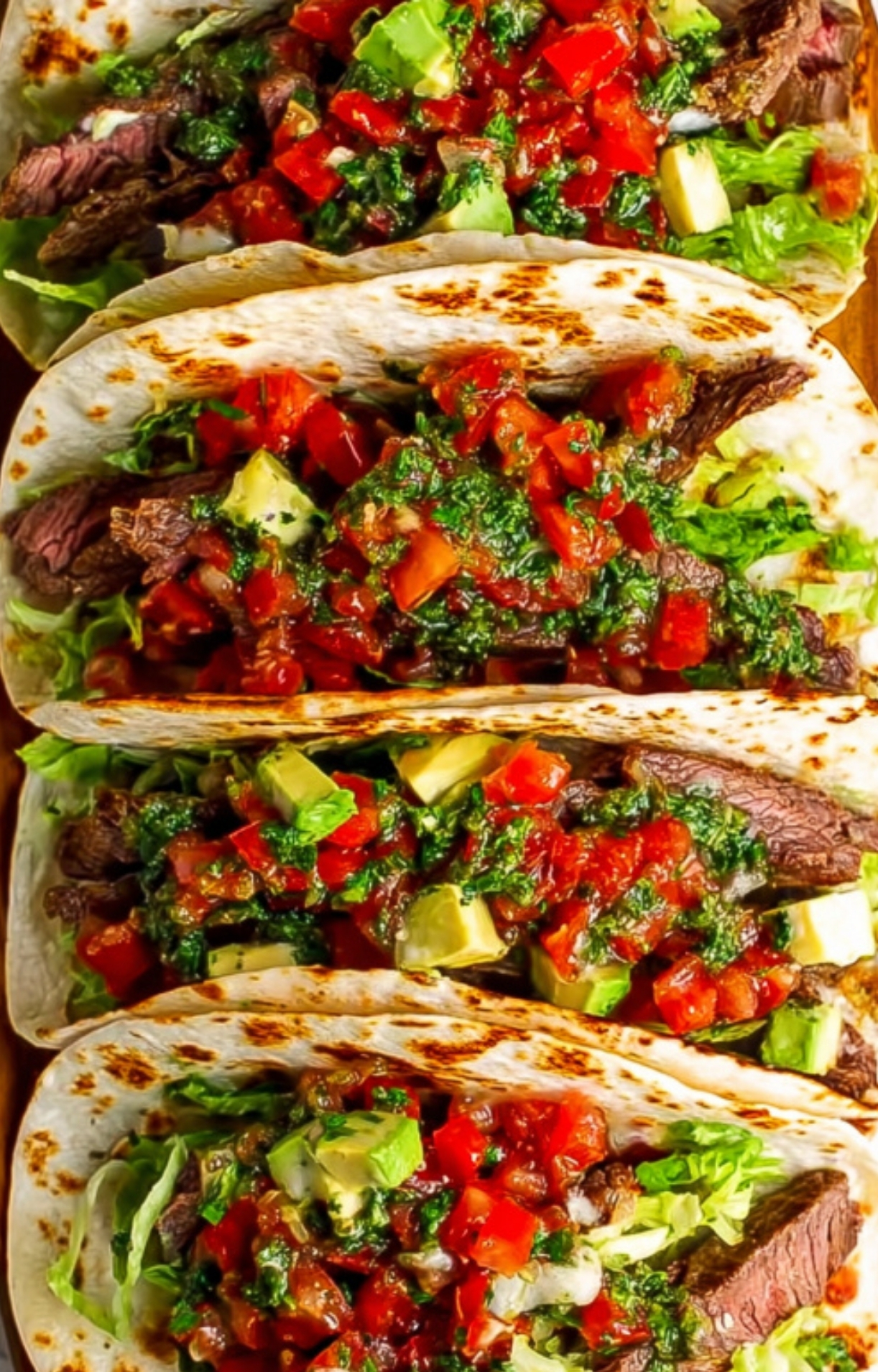 Steak tacos packed with lettuce, avocado, diced tomatoes, and herby chimichurri, ready for taco night, backyard BBQs, or a quick dinner.