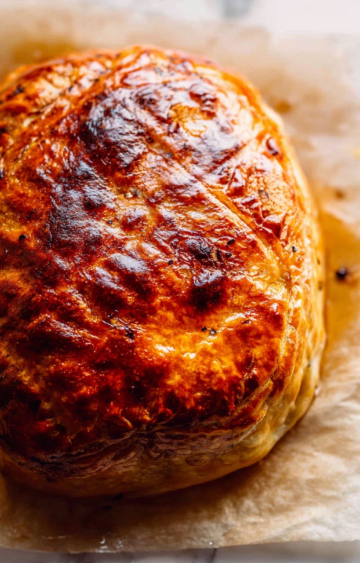 A whole beef wellington with tenderloin, perfectly baked to a golden brown crust, resting on parchment paper for a holiday feast.