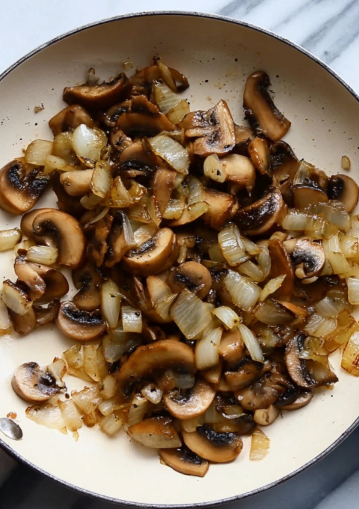Mushrooms and onions sautéed together in a skillet, ready for the classic duxelles layer in beef wellington recipes.