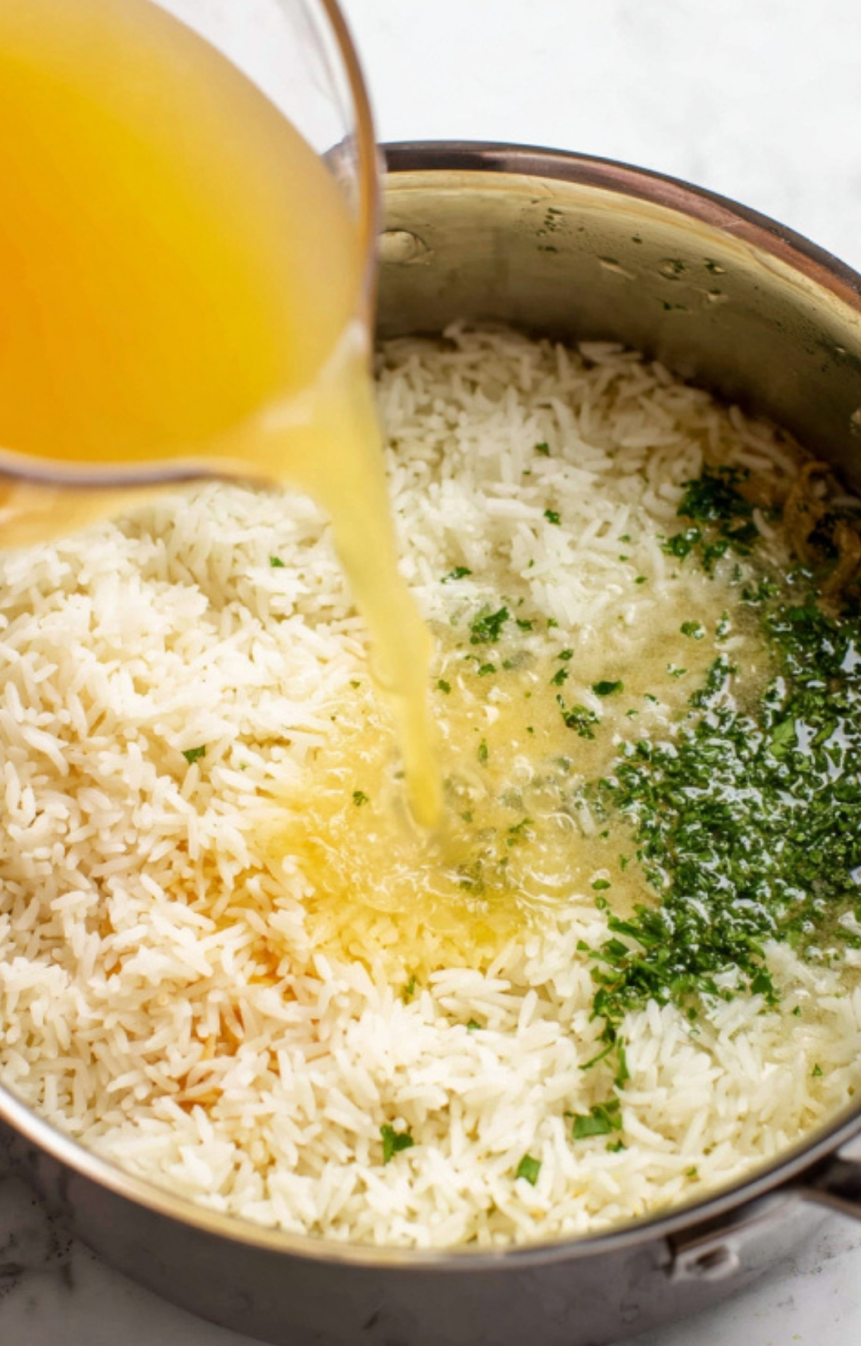 Pouring savory broth over cooked rice with herbs, step for a simple one-pot shrimp and rice dinner