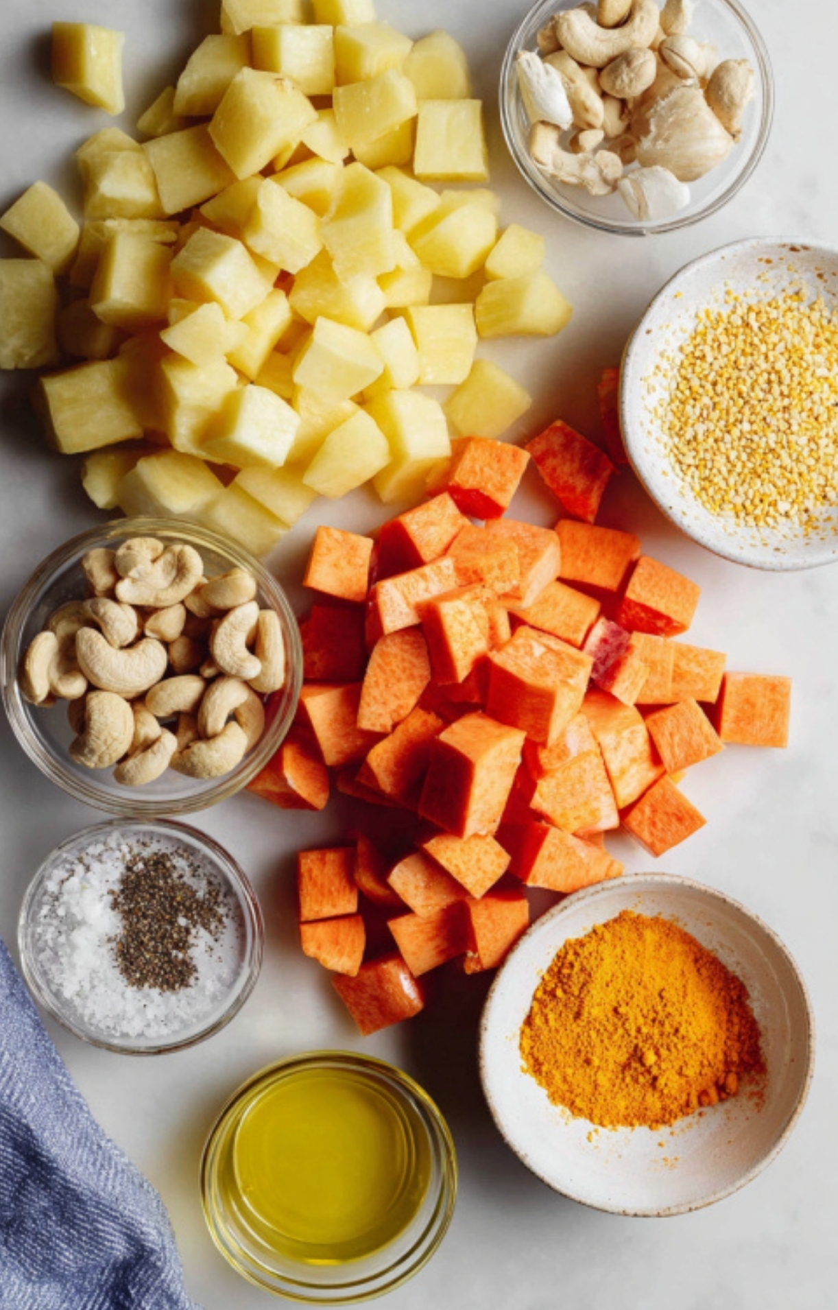 Chopped potatoes, sweet potatoes, cashews, and seasonings arranged on a countertop, showing the healthy plant-based ingredients for a weeknight meal for family.