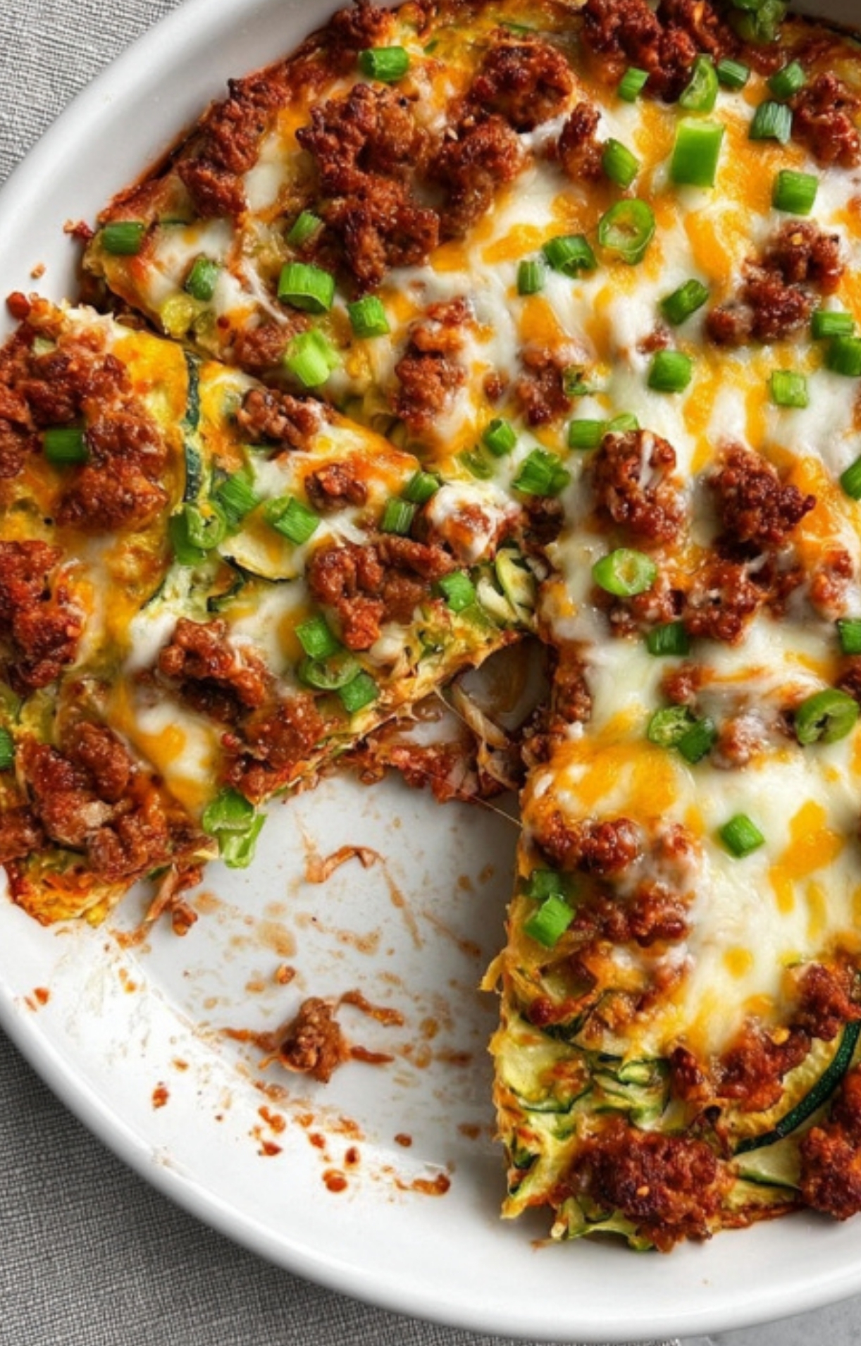 Golden-baked pizza casserole with beef, cheese, zucchini, and green onions, one slice served from the pan