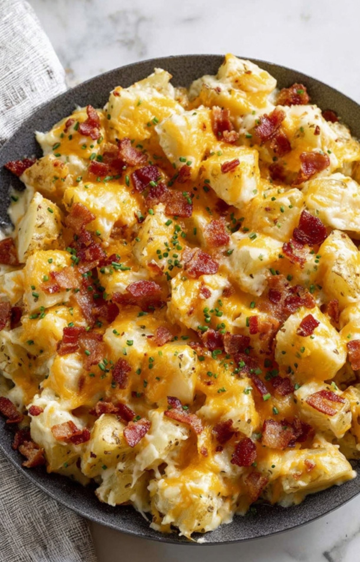 Cheddar cheese and bacon sprinkled over ranch potatoes, ready to bake for a cheesy potato casserole.