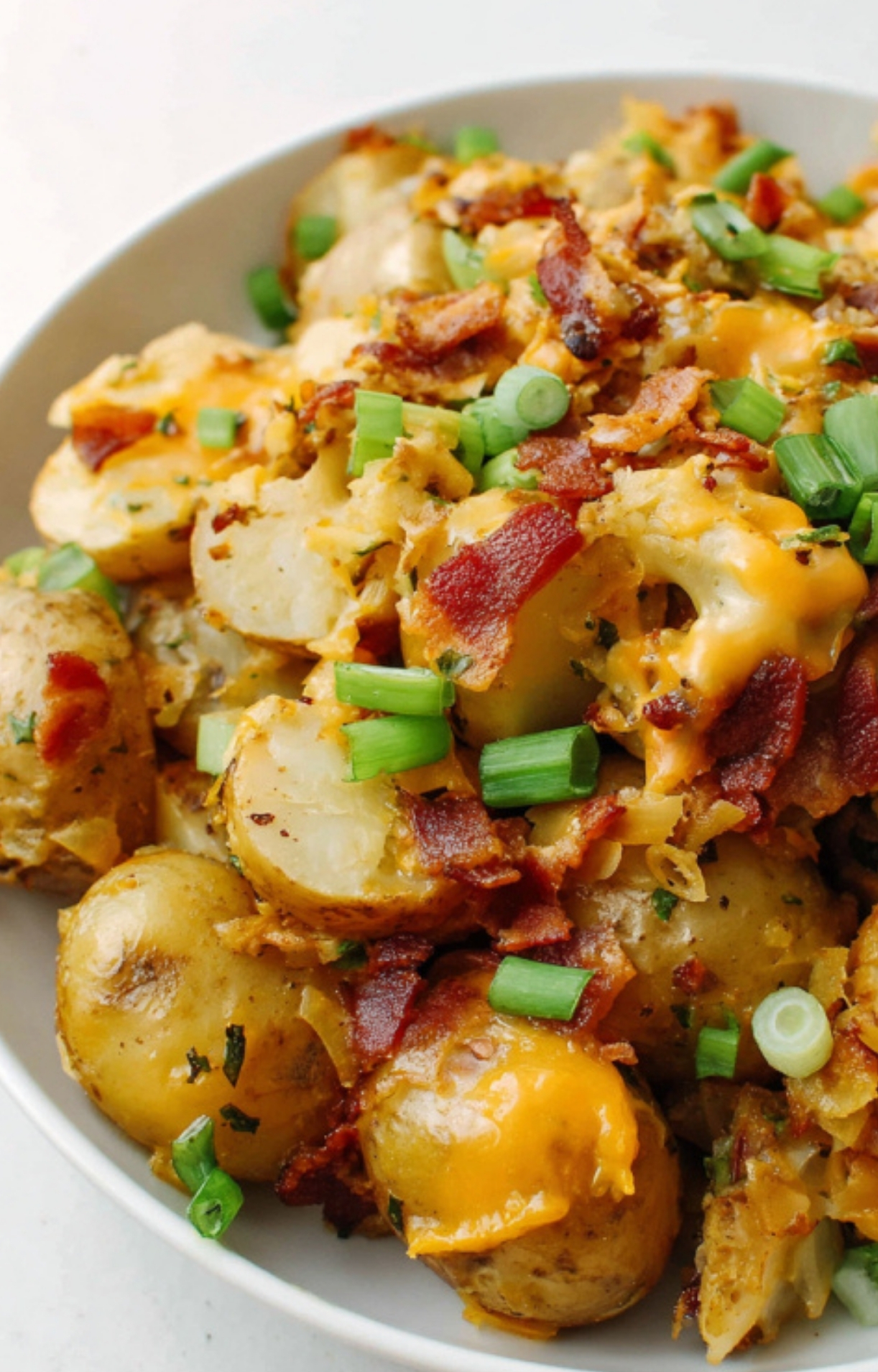 A bowl of slow cooker cheesy bacon ranch potatoes topped with crispy bacon and fresh green onions, a family favorite comfort food side.