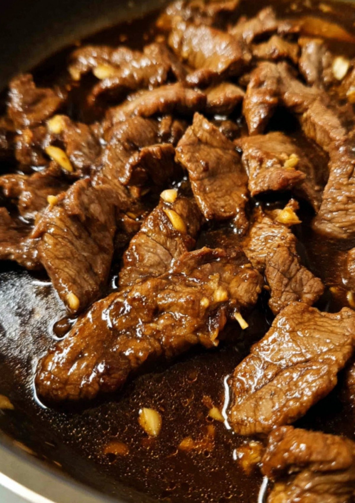 Tender beef strips simmering in a dark soy lemon garlic sauce for Beef Steak Filipino.