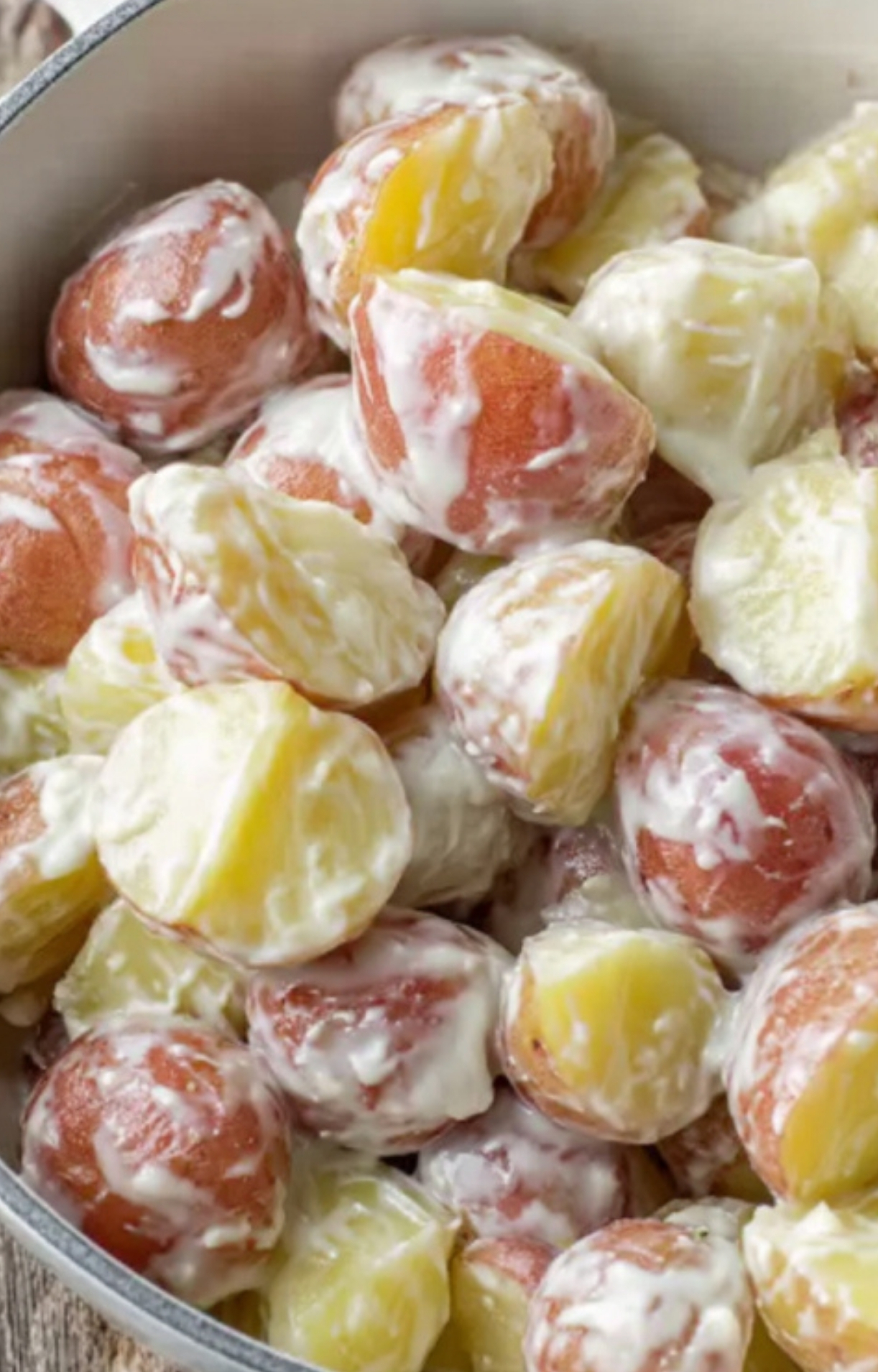 Red potatoes tossed in ranch sauce in a mixing bowl, ready to bake into a cheesy potato casserole.