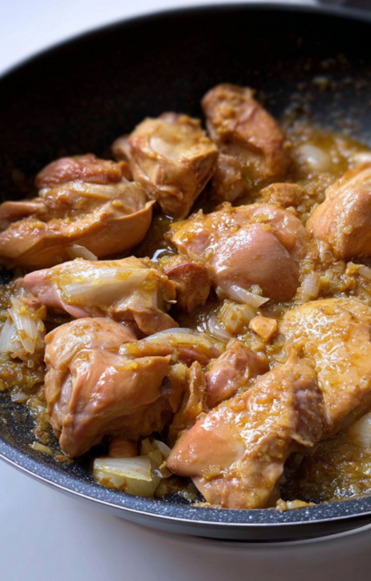Chicken pieces cooking with onions in a skillet. Step for making homemade chicken caldereta for any season.