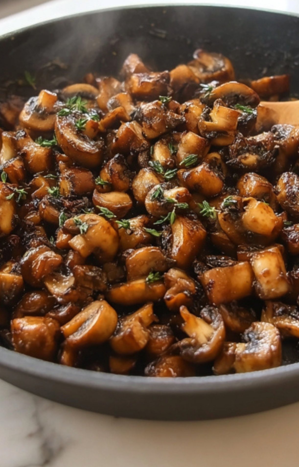 Chopped mushrooms cooking in a skillet with fresh thyme, perfect for making mushroom duxelles for a gluten free beef wellington recipe.
