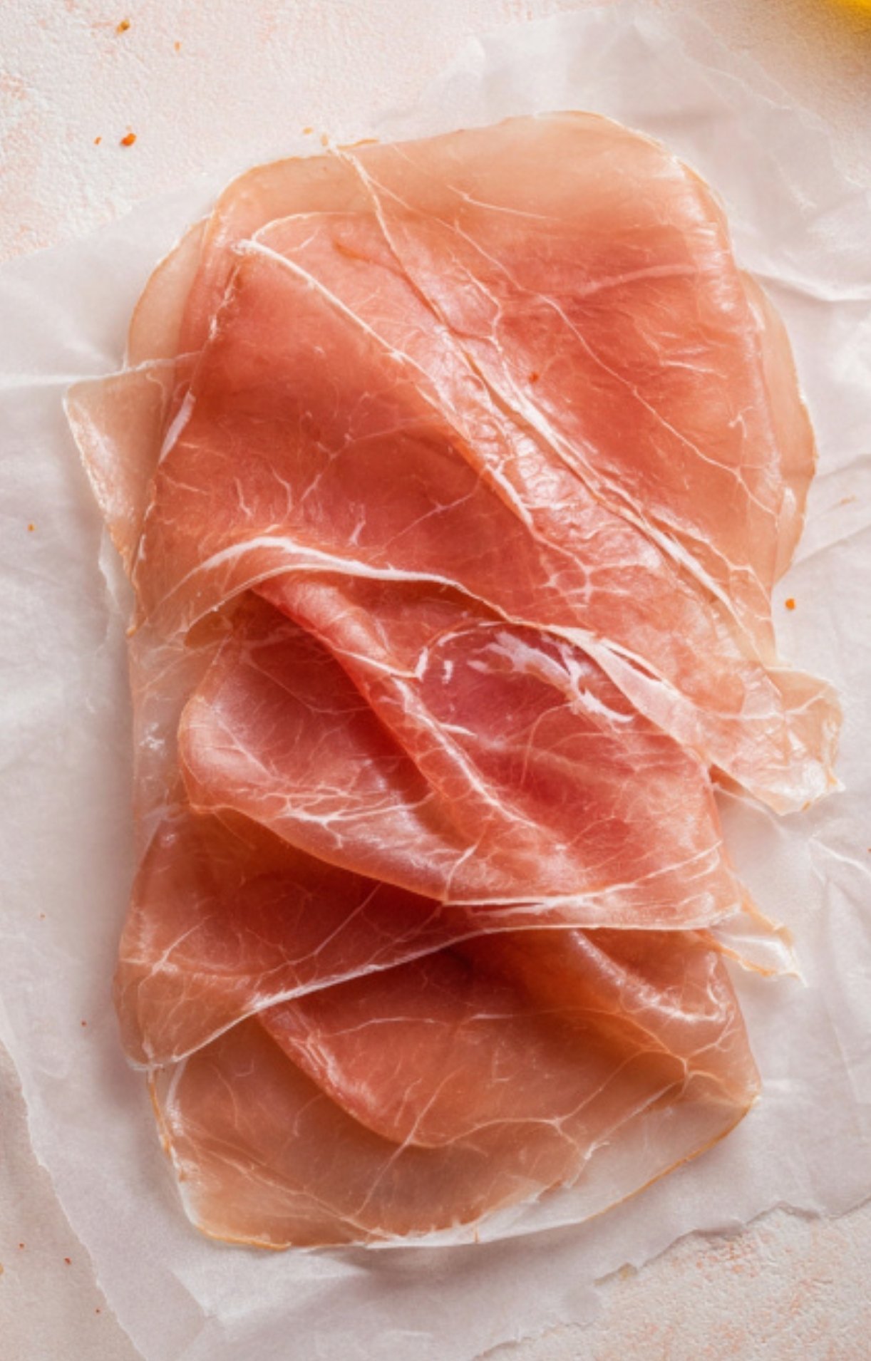 Thin slices of prosciutto arranged on parchment, perfect for adding a savory layer to beef Wellington recipes.