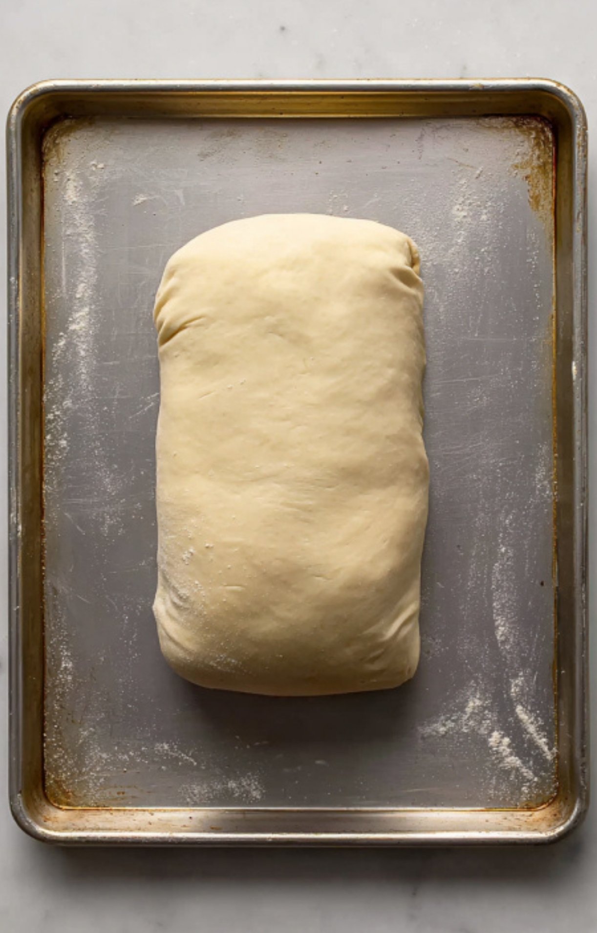 Beef wellington fully wrapped in plain puff pastry, resting on a baking sheet and ready to be decorated and baked. Essential preparation for making a classic beef wellington for special occasions.