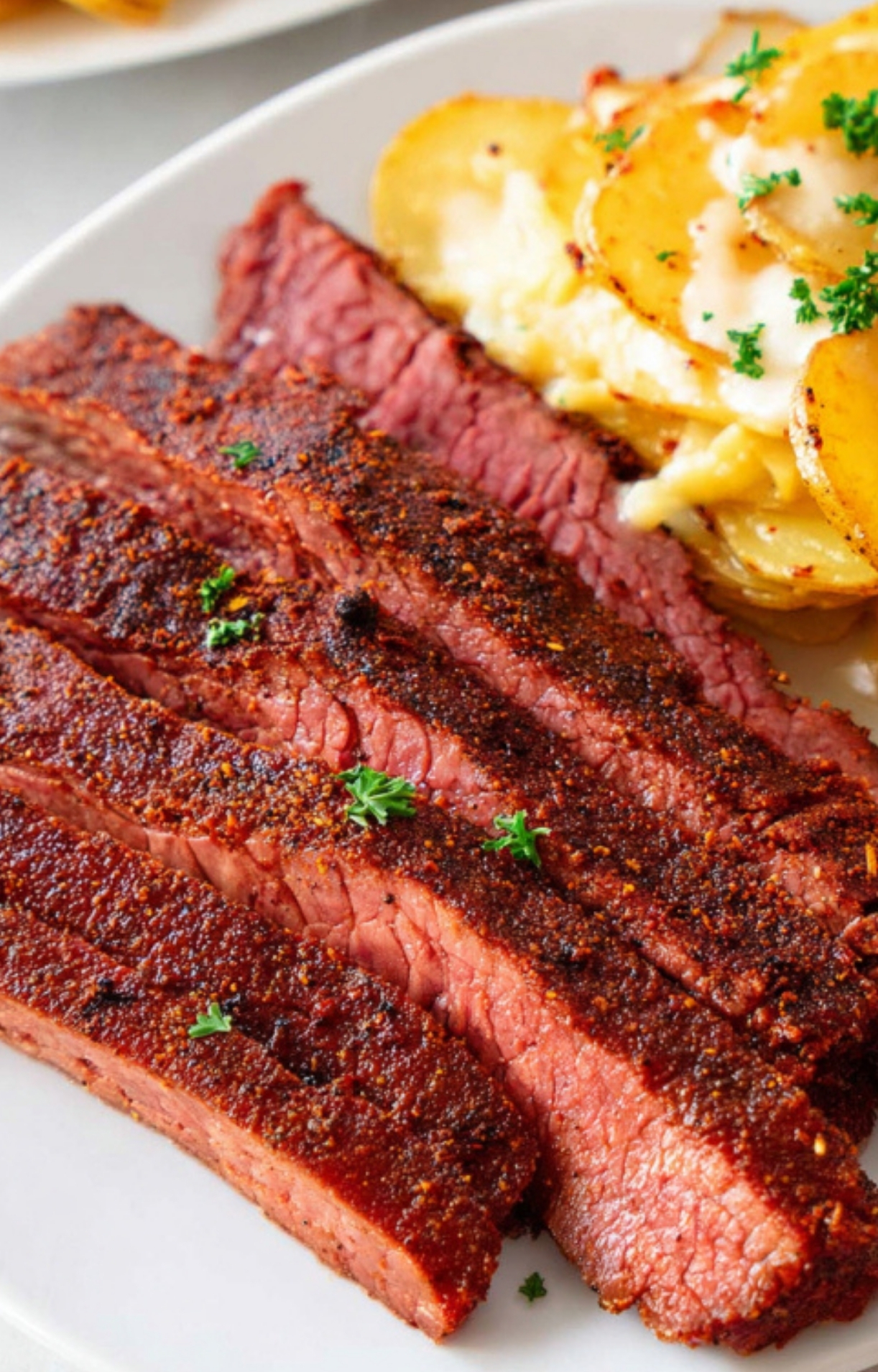 Slices of smoky flank steak next to scalloped potatoes, garnished with parsley, a delicious choice for family dinners and gatherings.