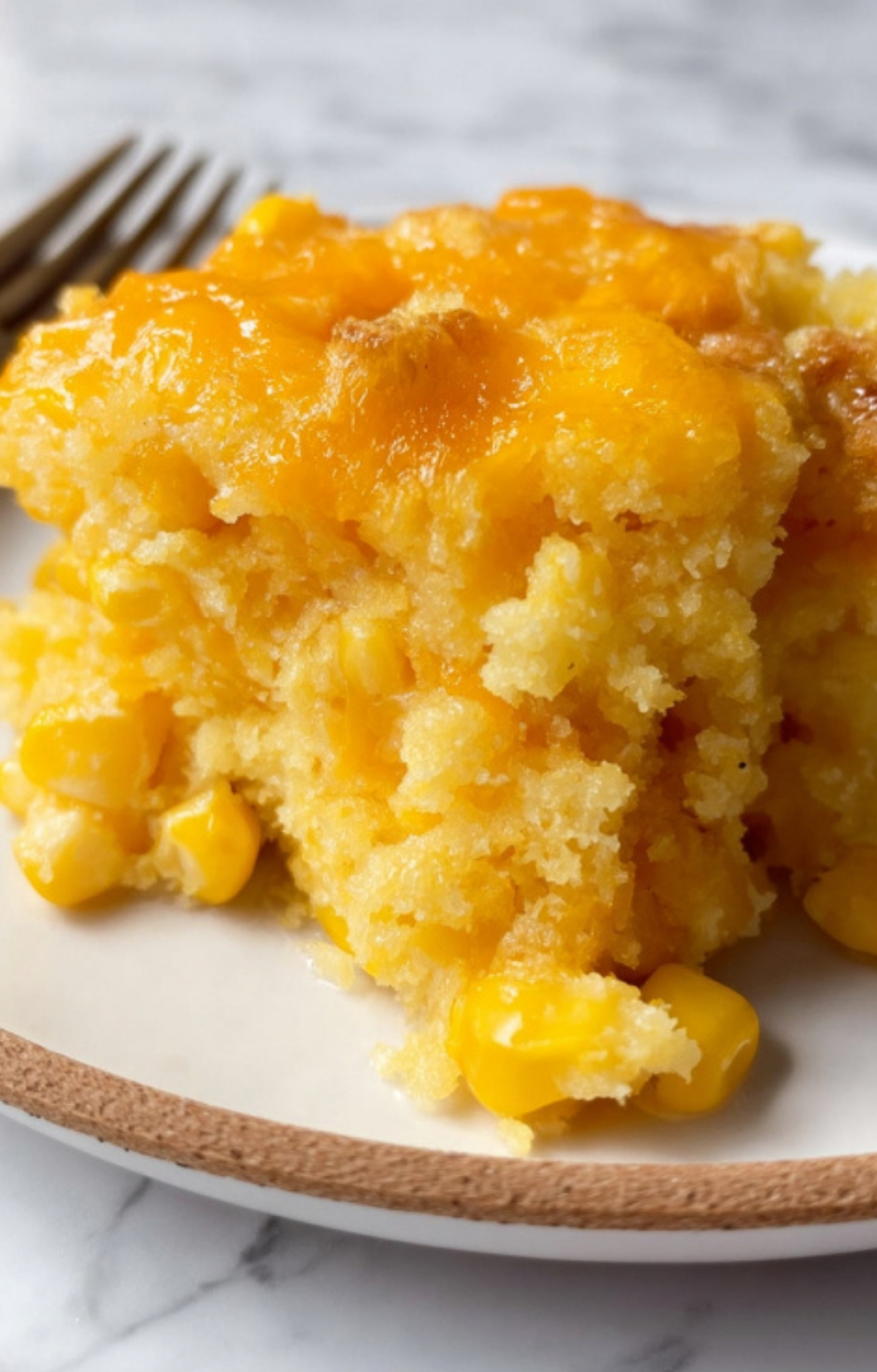 A close up of a cheesy, moist piece of baked corn casserole on a plate, ready to serve for the holidays