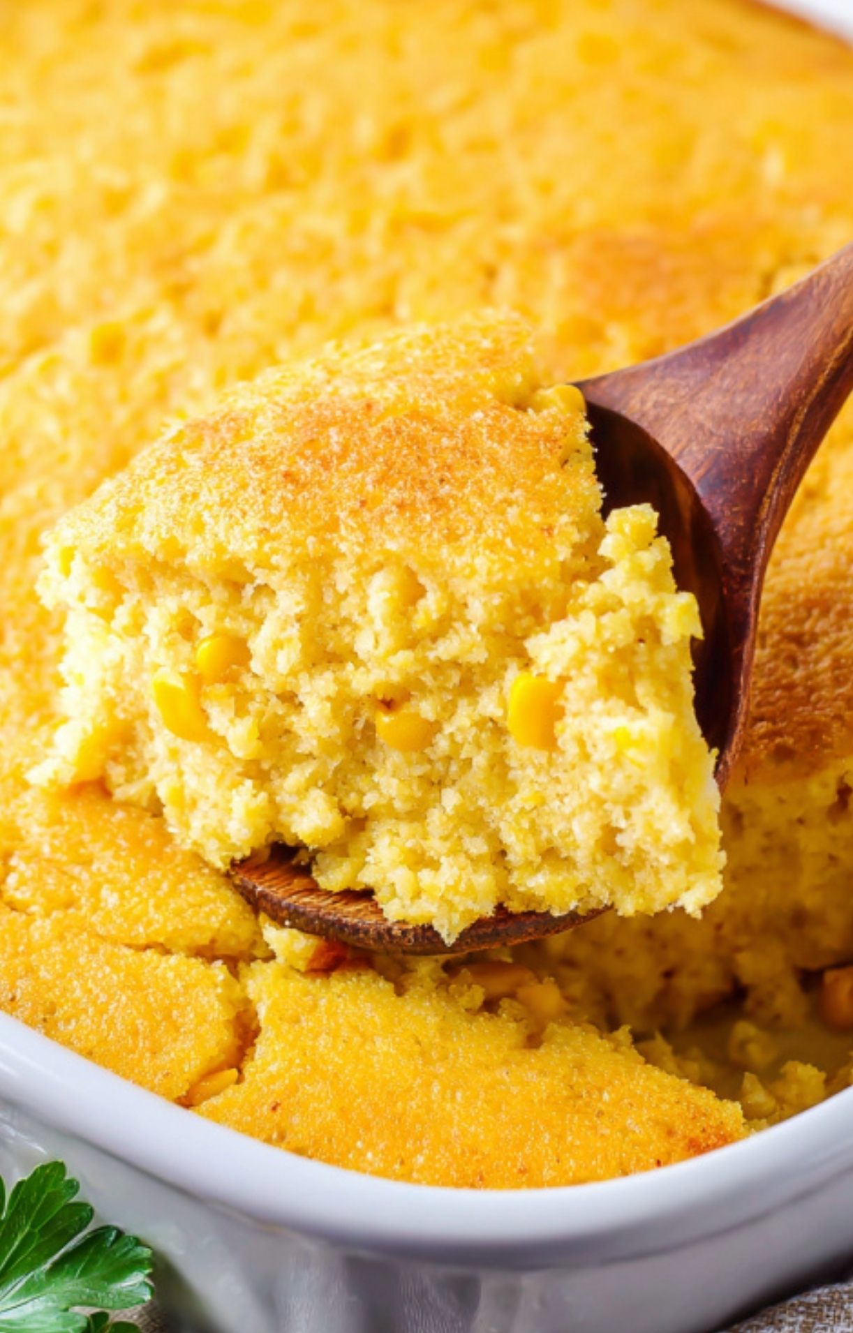 A wooden spoon lifting a fluffy, golden piece of Corn Casserole Jiffy Easy from the baking dish, showing a tender texture and real corn kernels, perfect for holiday dinners.
