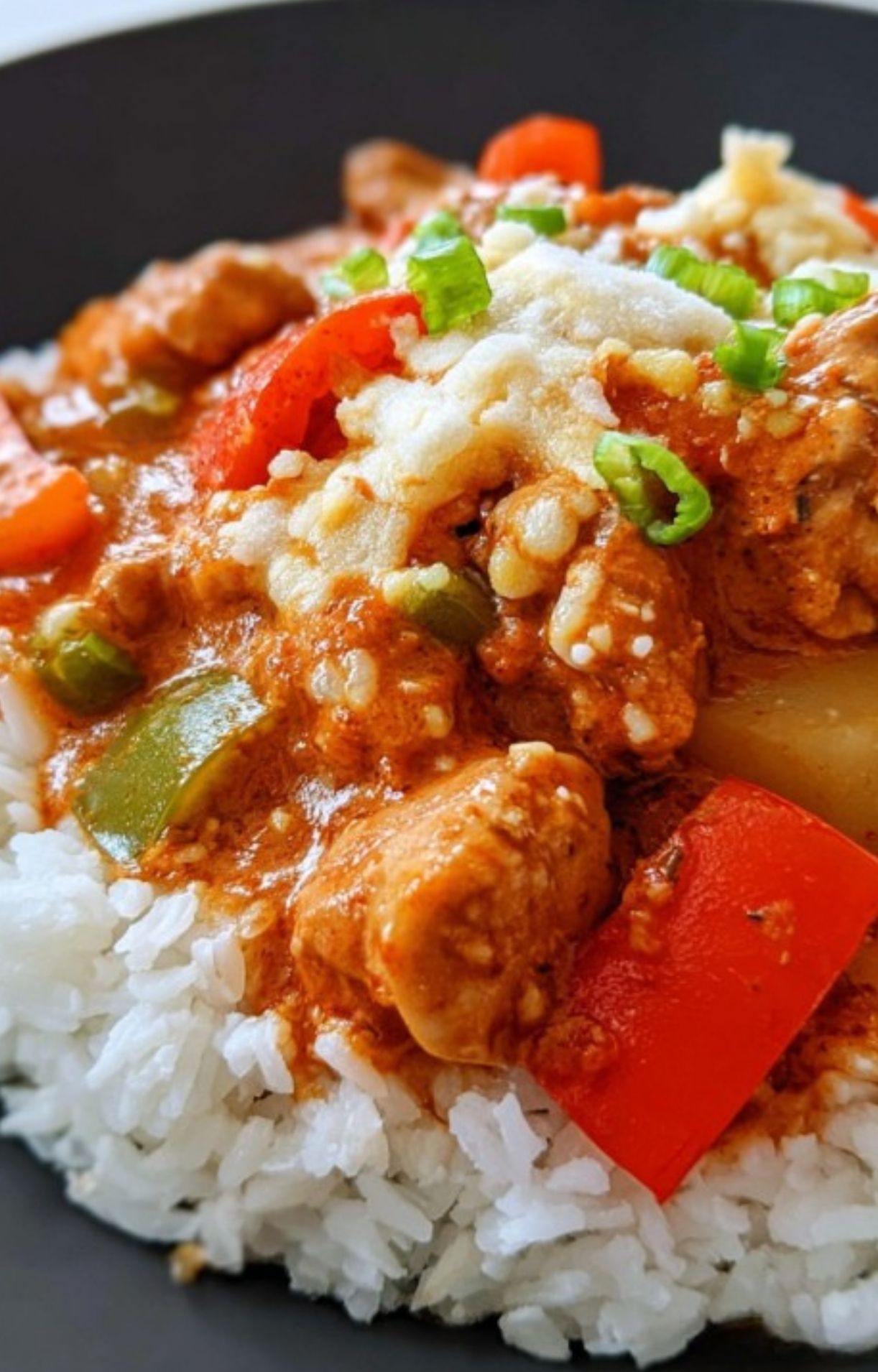 Chicken caldereta on white rice, topped with cheese and green onions. Great weeknight dinner or lunch idea.