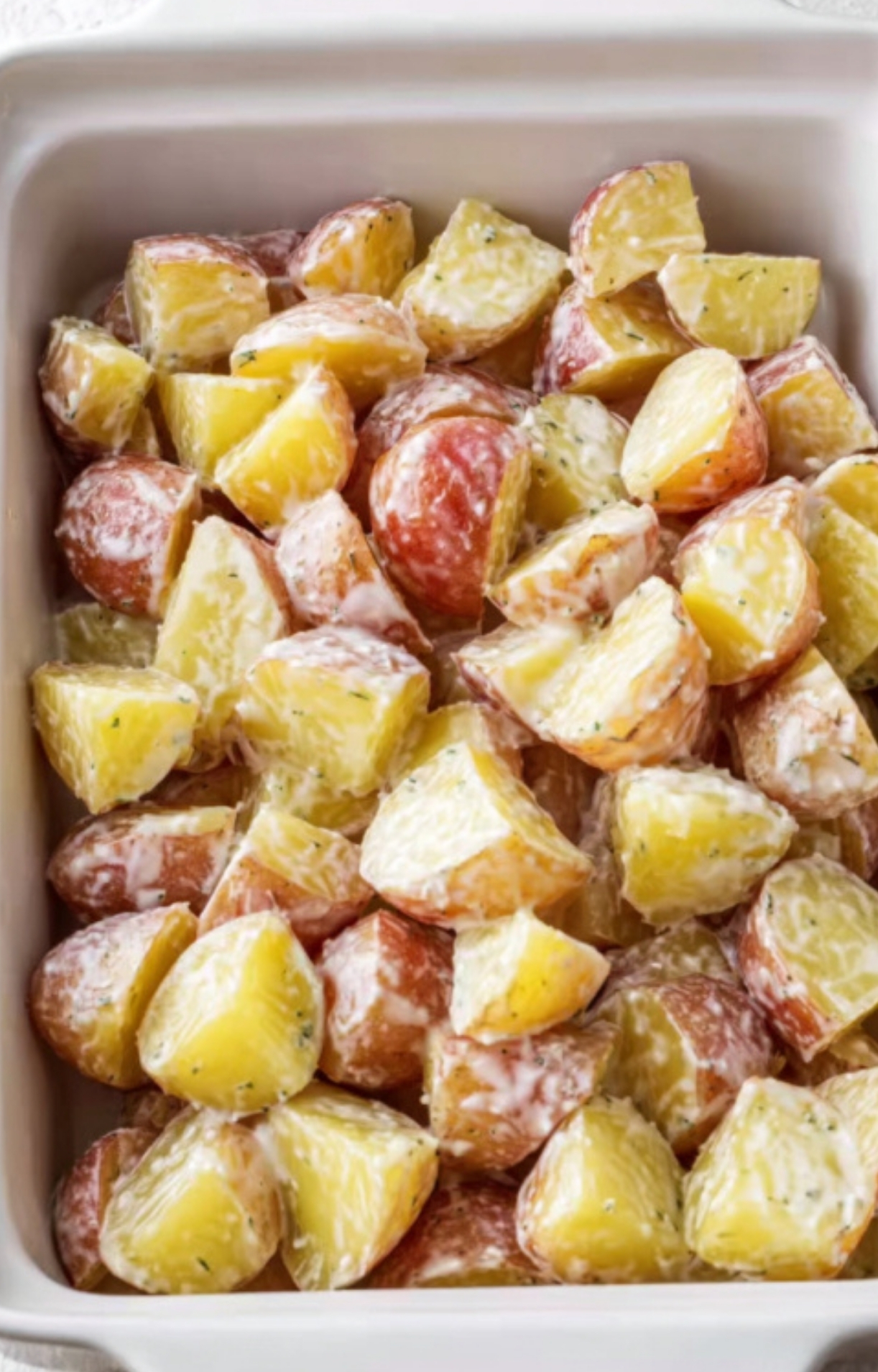Diced potatoes tossed in ranch sauce arranged in a casserole dish, prepped and ready for cheese topping.
