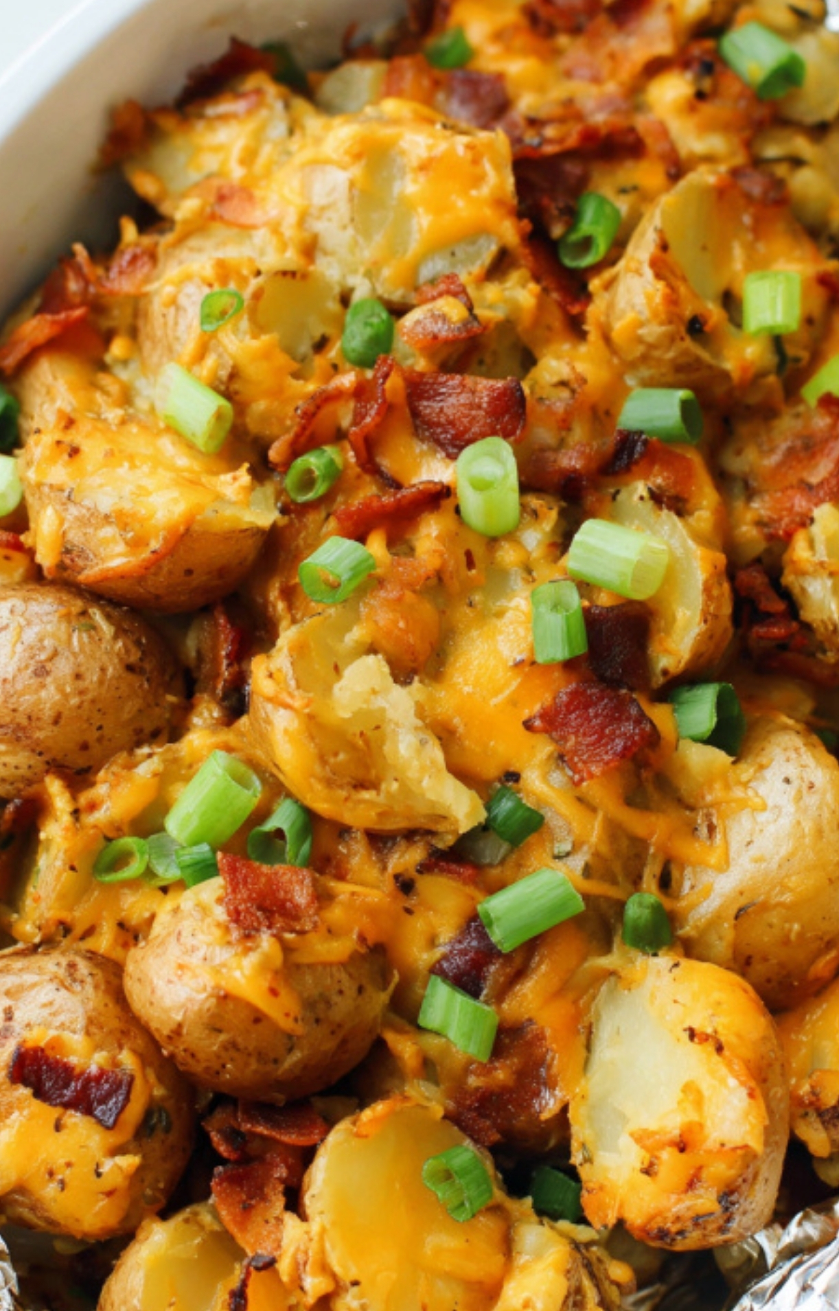 Golden potatoes mixed with melted cheddar, bacon, and green onions in a bowl, showing the rich texture of this crock pot side dish.