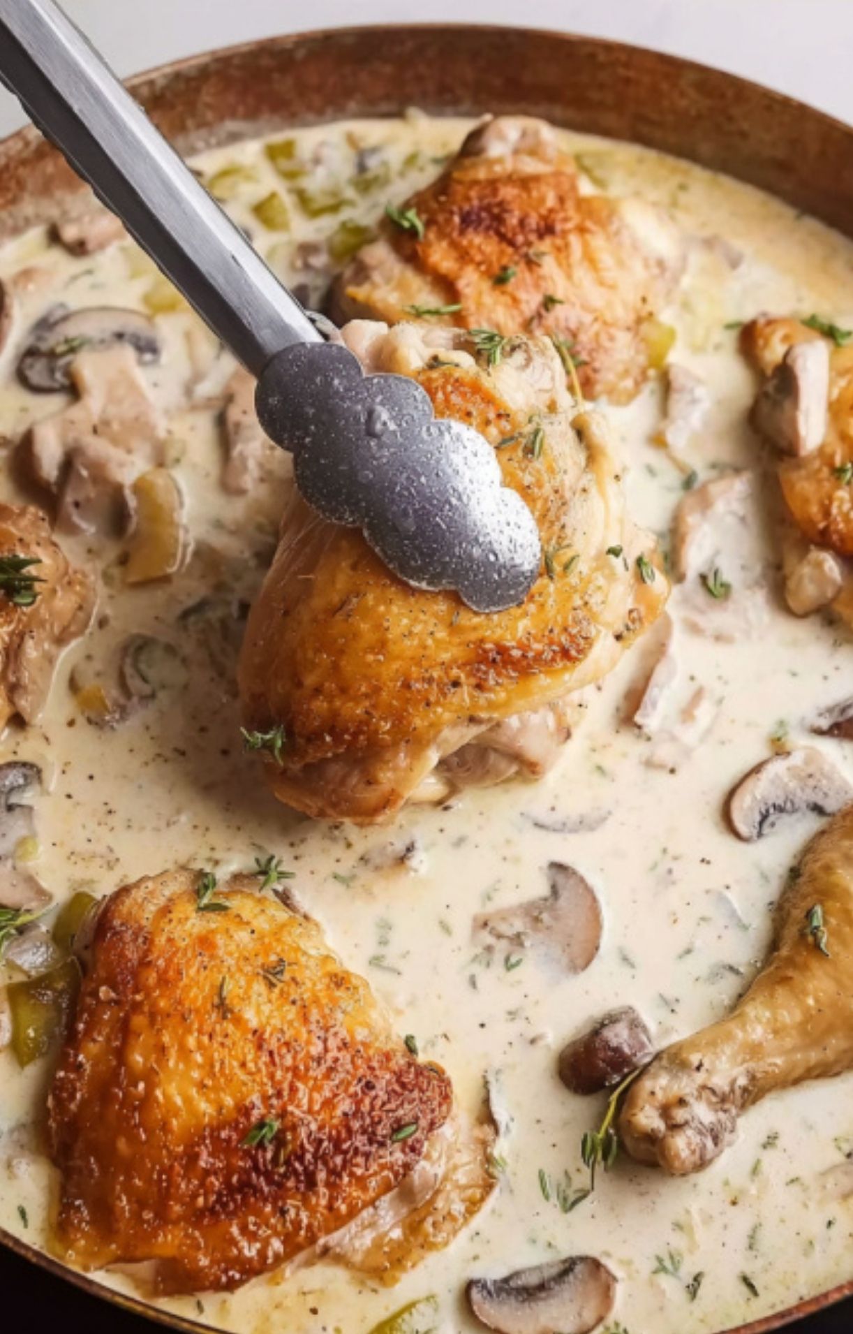 Chicken pieces with crispy skin in a skillet with rich creamy mushroom sauce and fresh thyme.