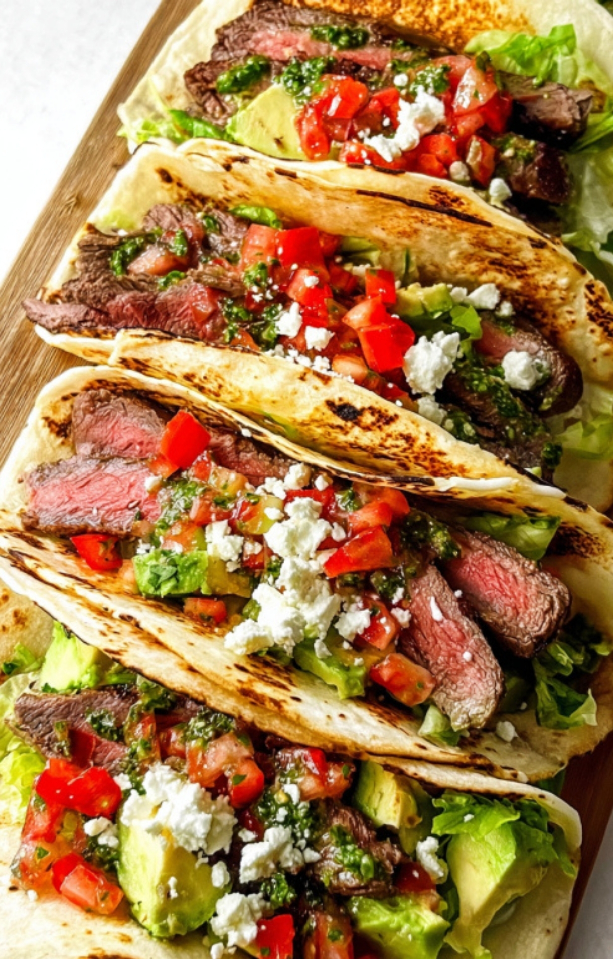 Charred tortillas stuffed with grilled shaved steak, diced tomatoes, feta cheese, and zesty chimichurri, a quick and festive taco recipe for any season.
