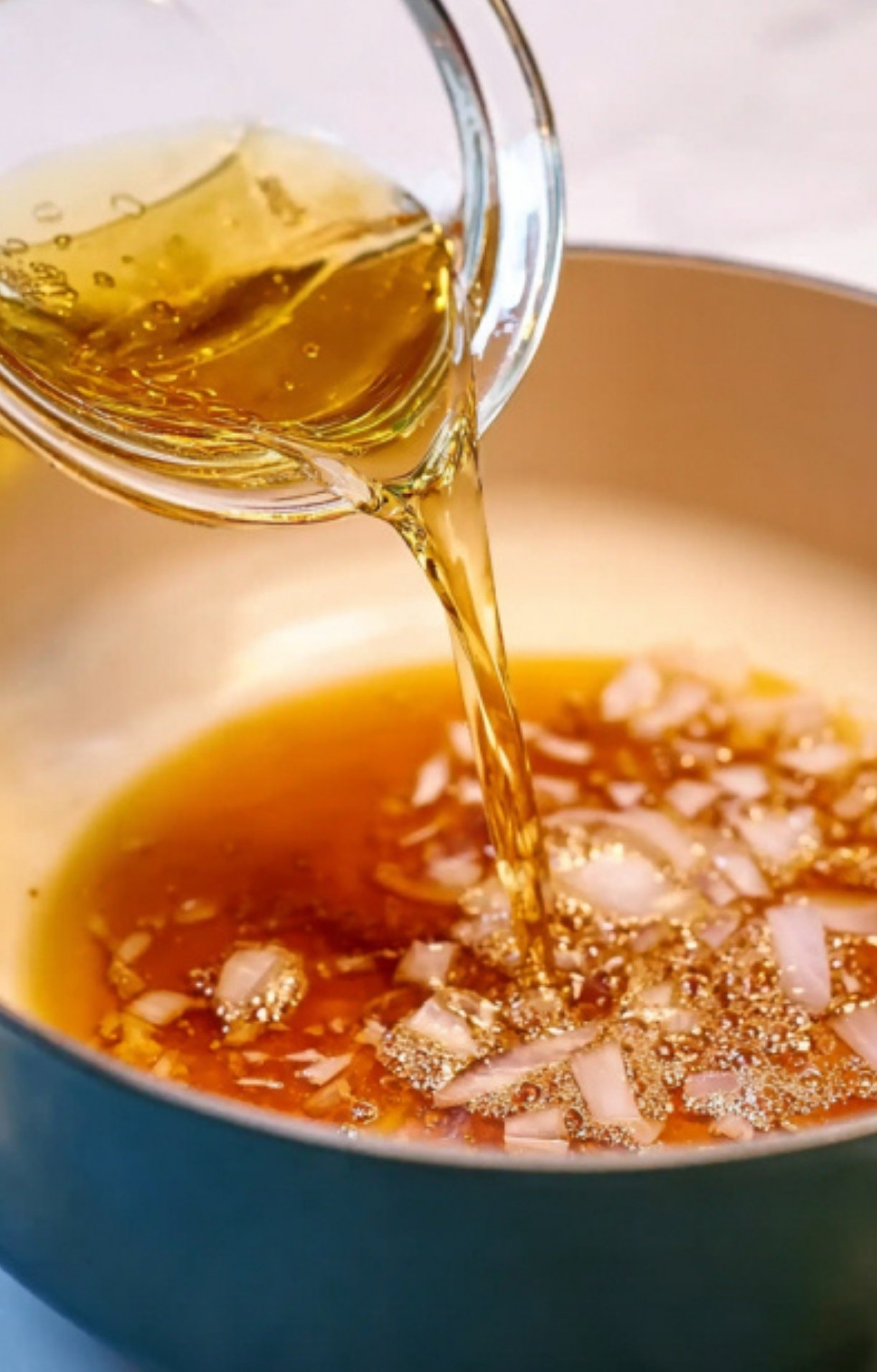 Pouring broth over sautéed onions to start a flavorful red wine sauce, a must-have step for gourmet beef dishes and Christmas dinner recipes.