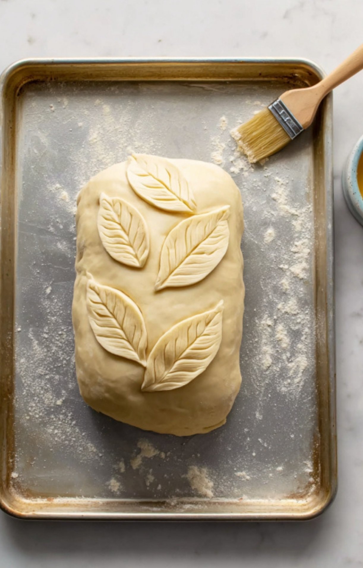 Unbaked beef wellington wrapped in puff pastry and decorated with pastry leaves, set on a baking tray and brushed with egg wash. A step showing how to prepare this classic beef wellington for baking, perfect for holiday entertaining.