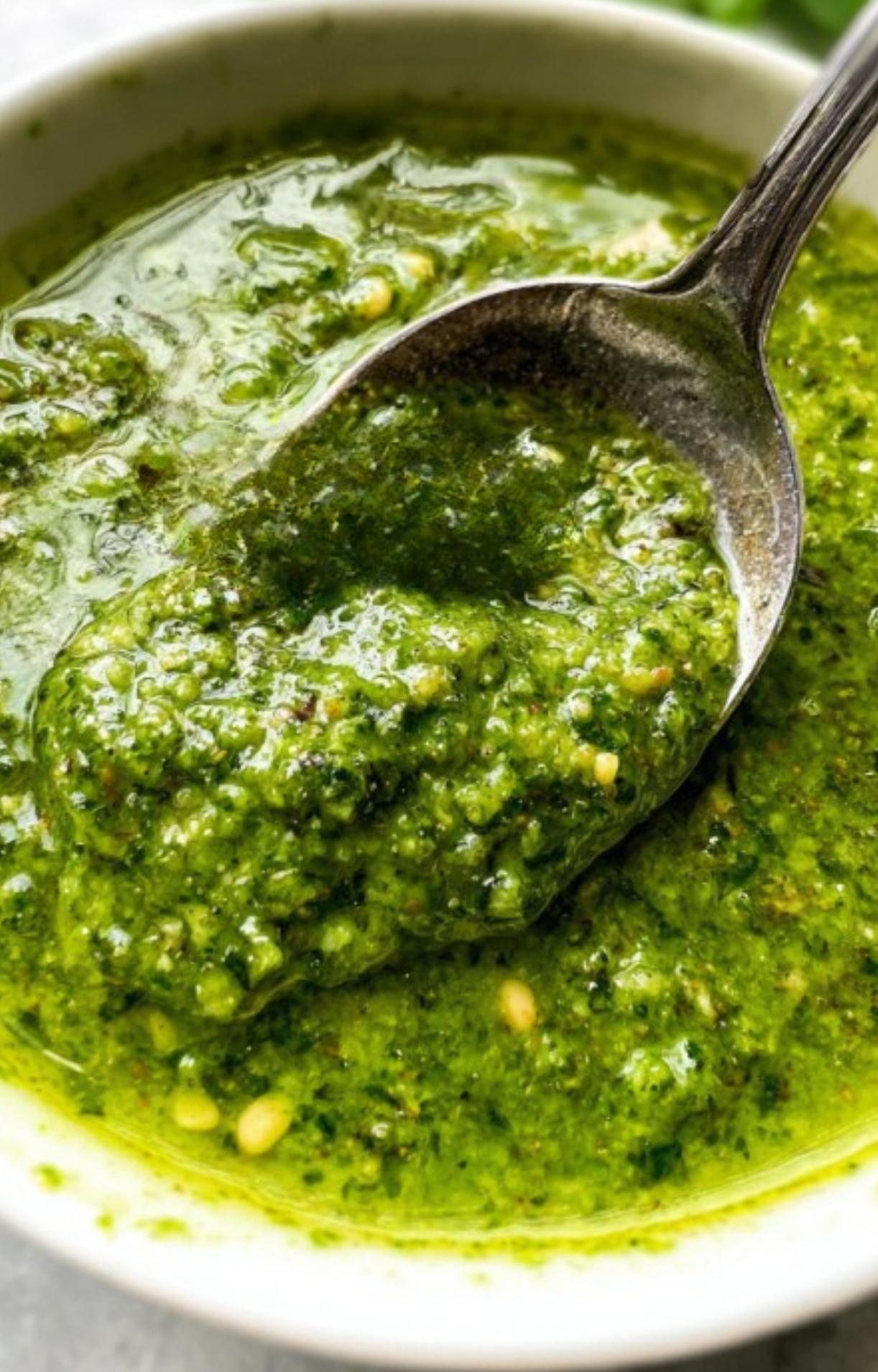 Close-up of a spoonful of vibrant green basil pesto in a bowl, showing a fresh homemade sauce for easy week night dinners, healthy pasta recipes, and Italian comfort food.