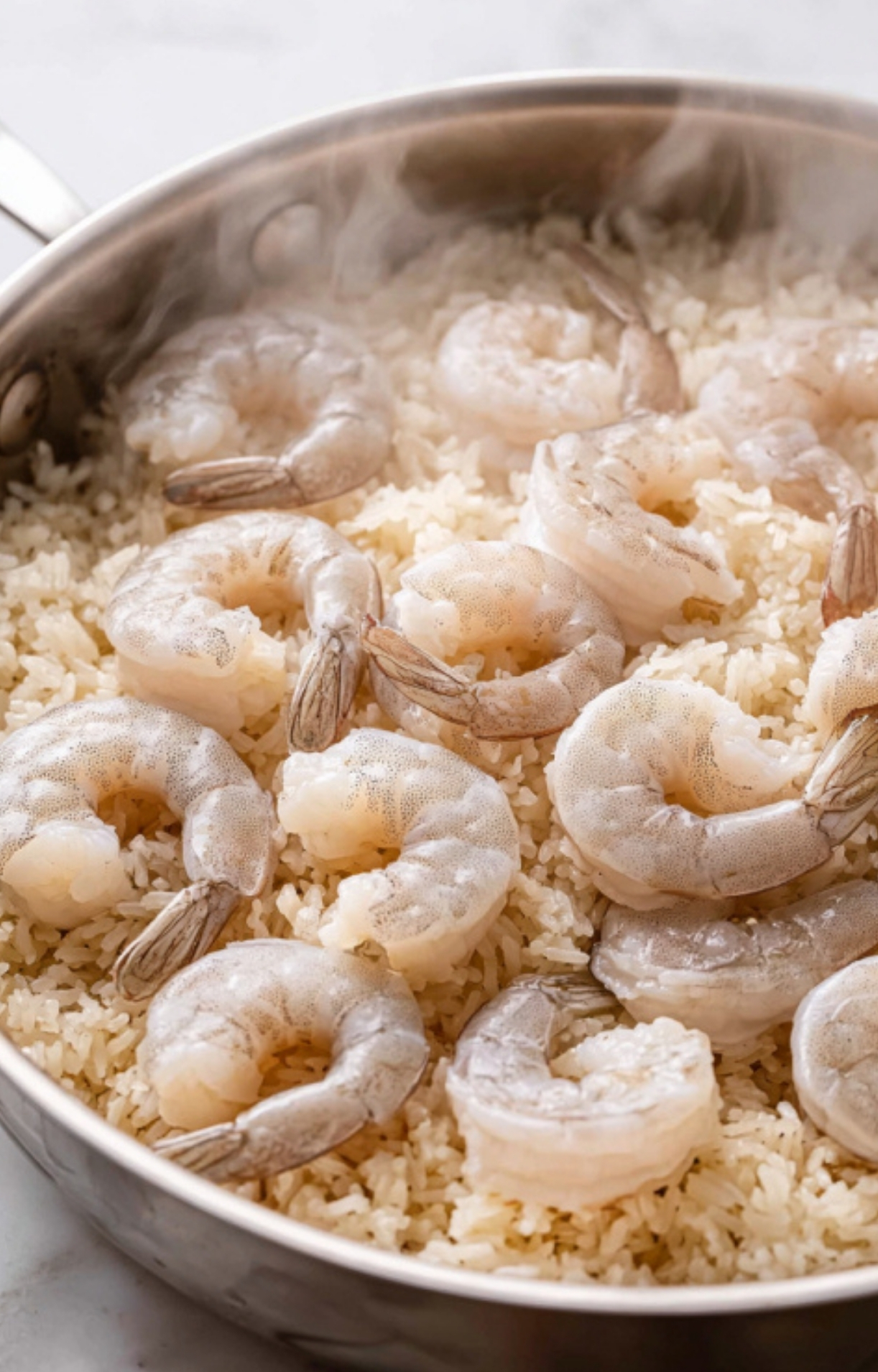 Raw shrimp arranged on a bed of steamed rice in a pan, showing the first step to a simple week night dinner, healthy seafood recipes, and family meal prep.