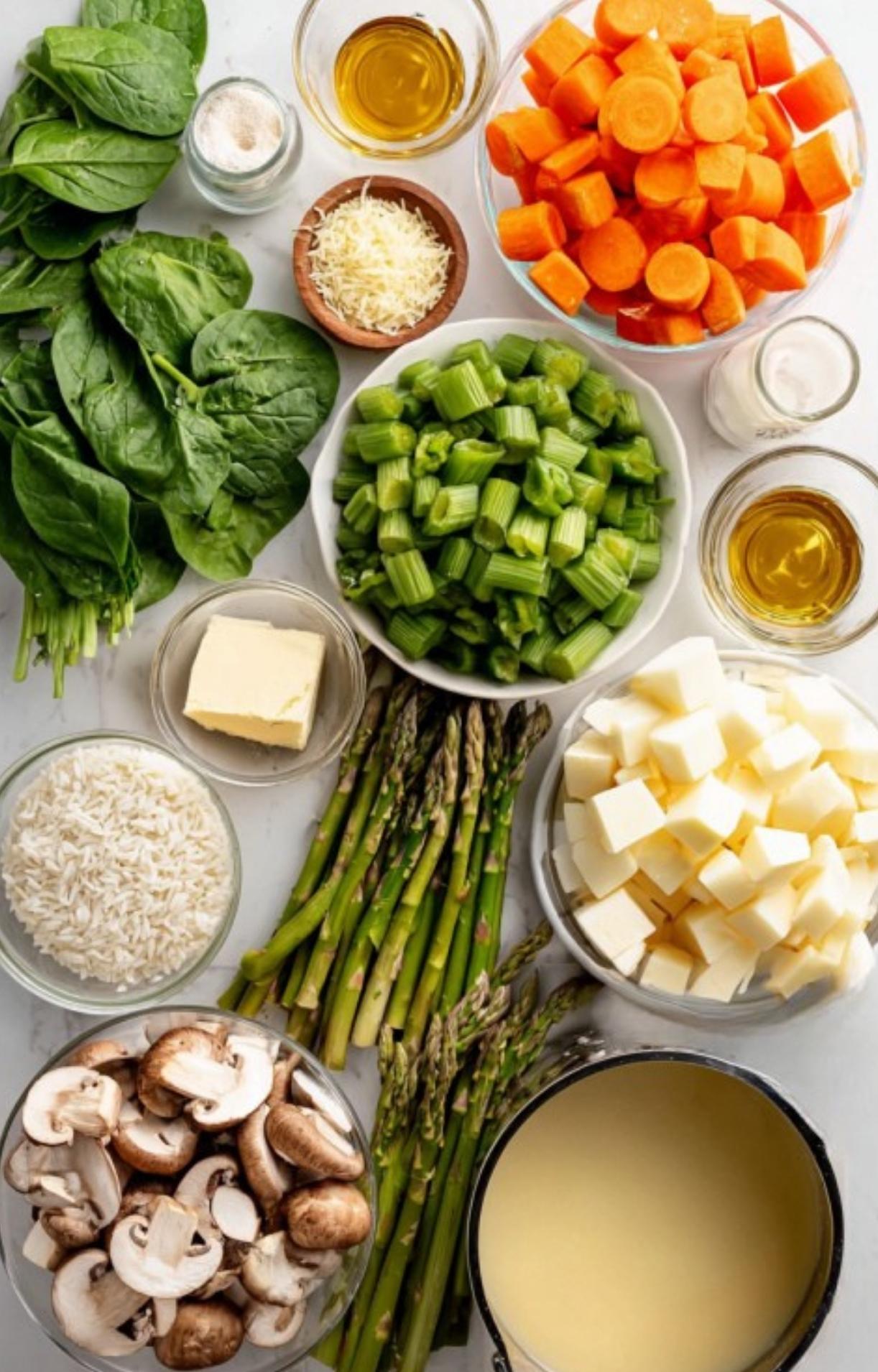 An overhead view of fresh soup ingredients: carrots, asparagus, potatoes, spinach, mushrooms, leeks, broth, and herbs. All ready for a healthy French spring soup recipe.
